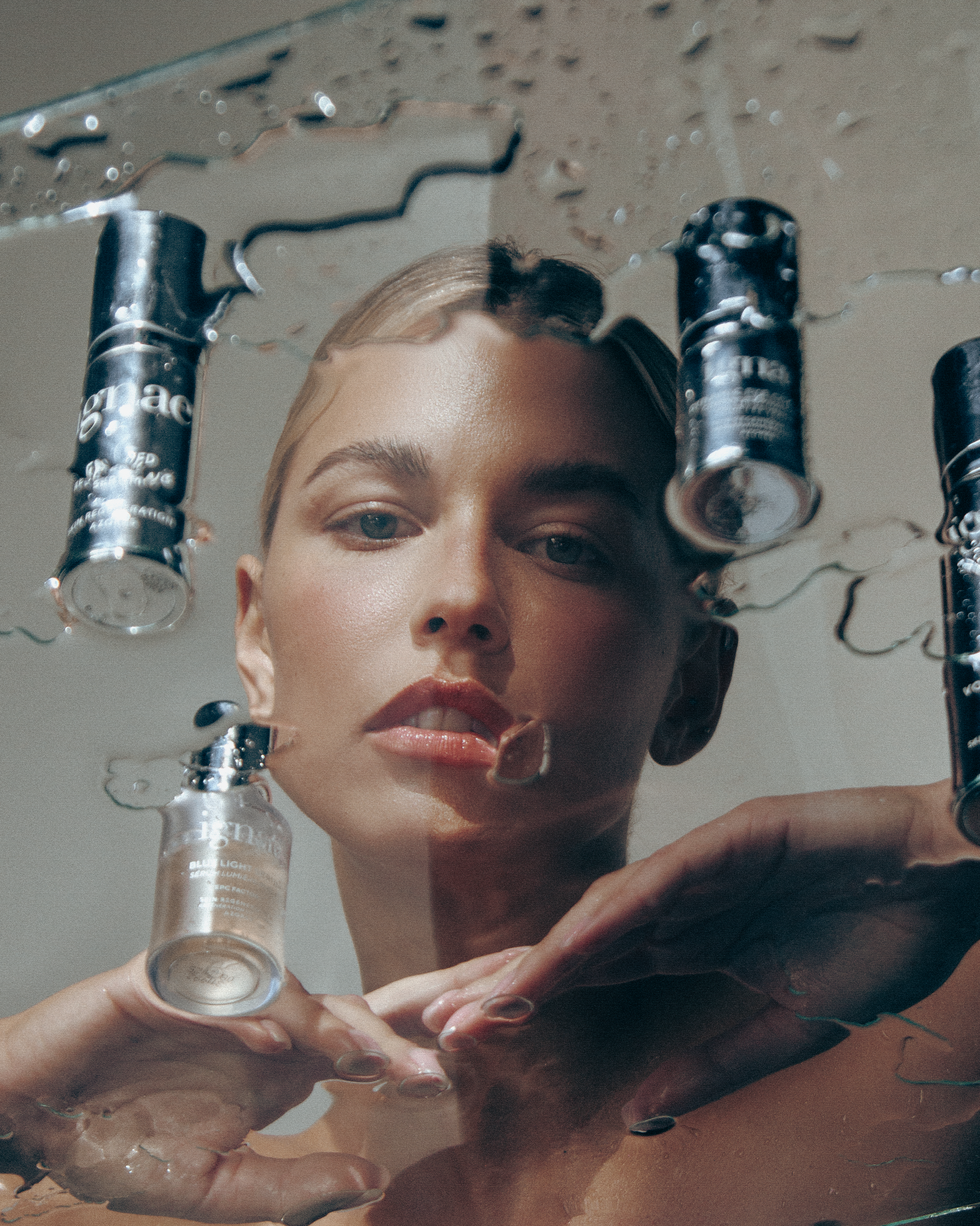 Close-up of a woman's face partially visible through a broken mirror, with a small vial labeled "Bell Light" held near her face, and her hand also visible.