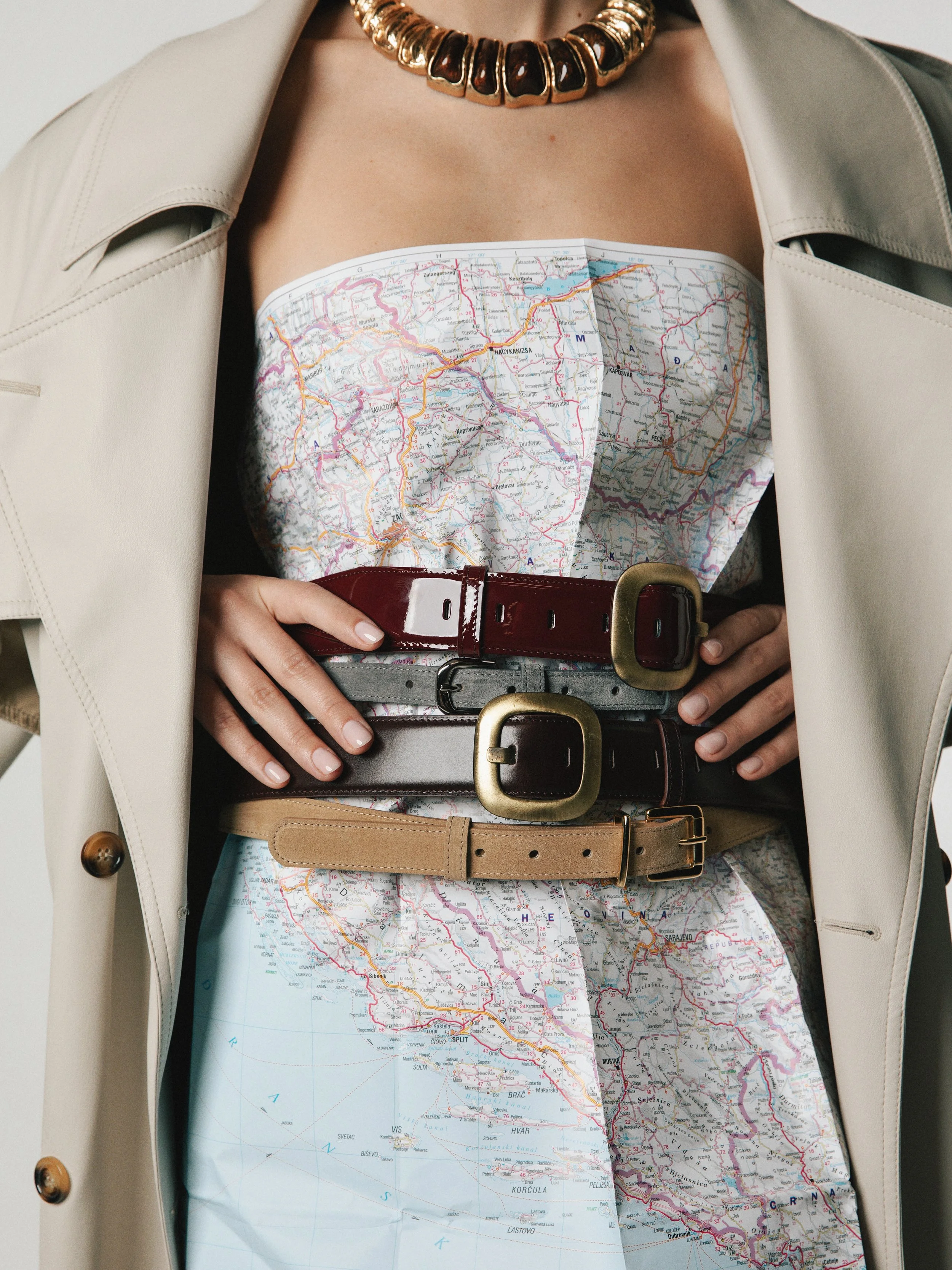 Person wearing a coat and a necklace, with their torso covered by a folded map of Croatia and neighboring countries, secured with multiple belts.
