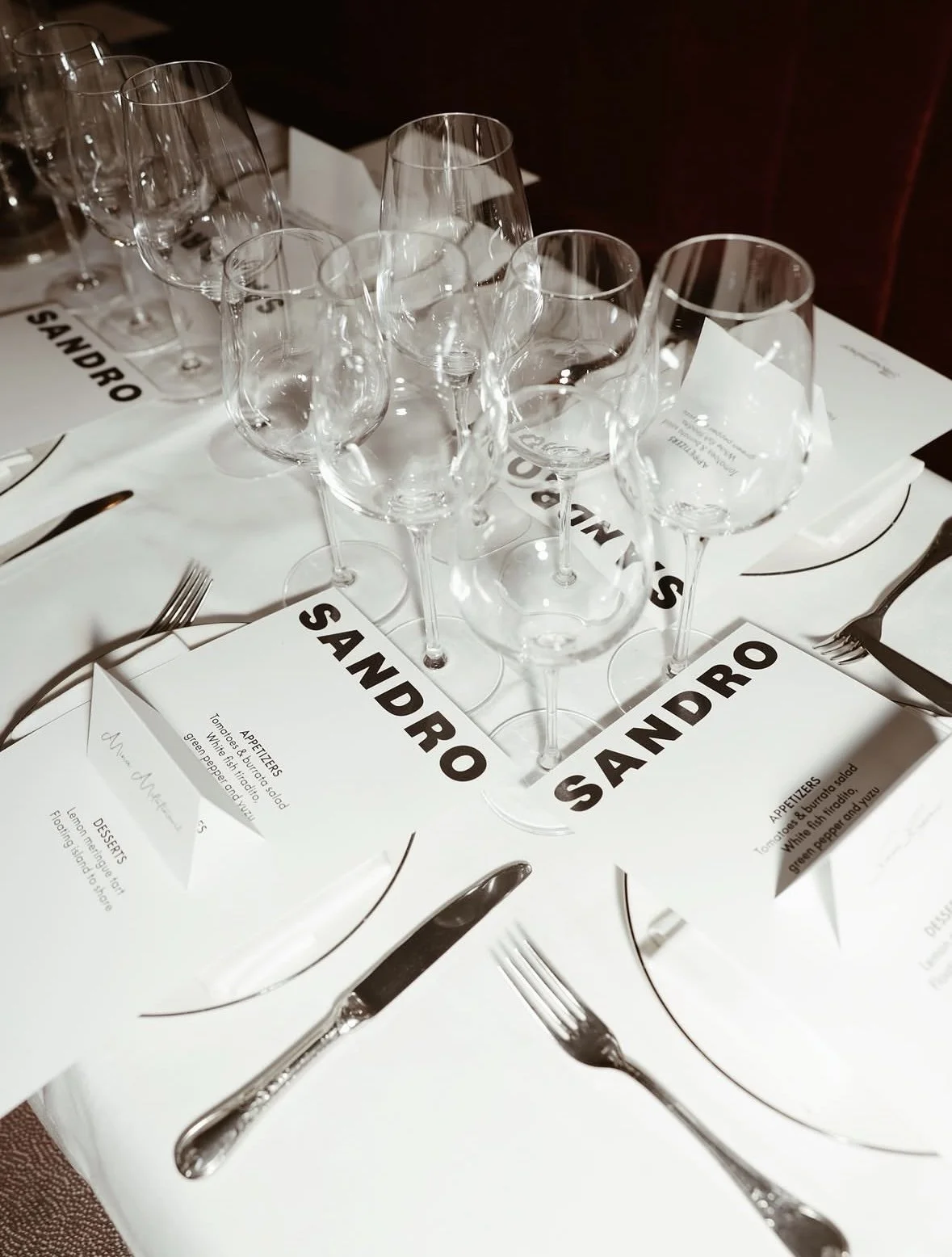 Elegant table setting with multiple empty wine glasses, silverware, white plates, and printed menus at a formal event.