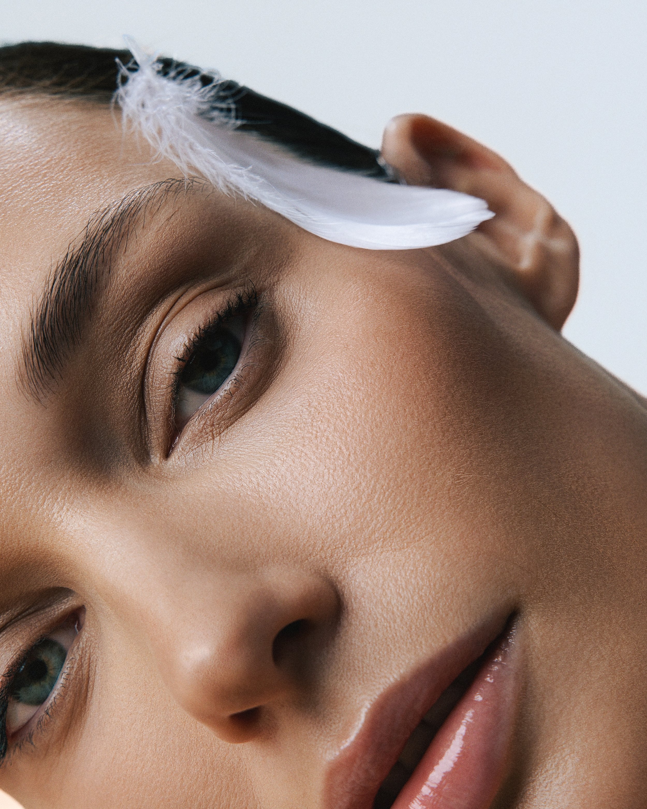 Close-up of a person's face with a hand holding a feather near the forehead.