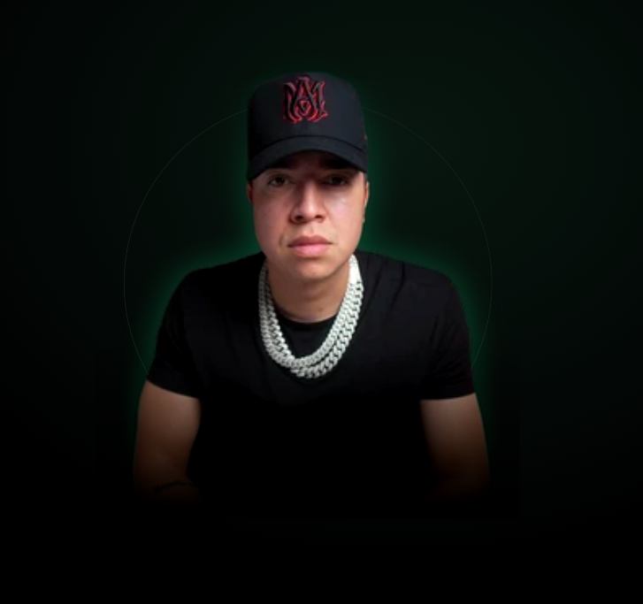 Young man wearing a black baseball cap with red embroidery, a black shirt, and multiple pearl necklaces, against a dark background with a green glow.