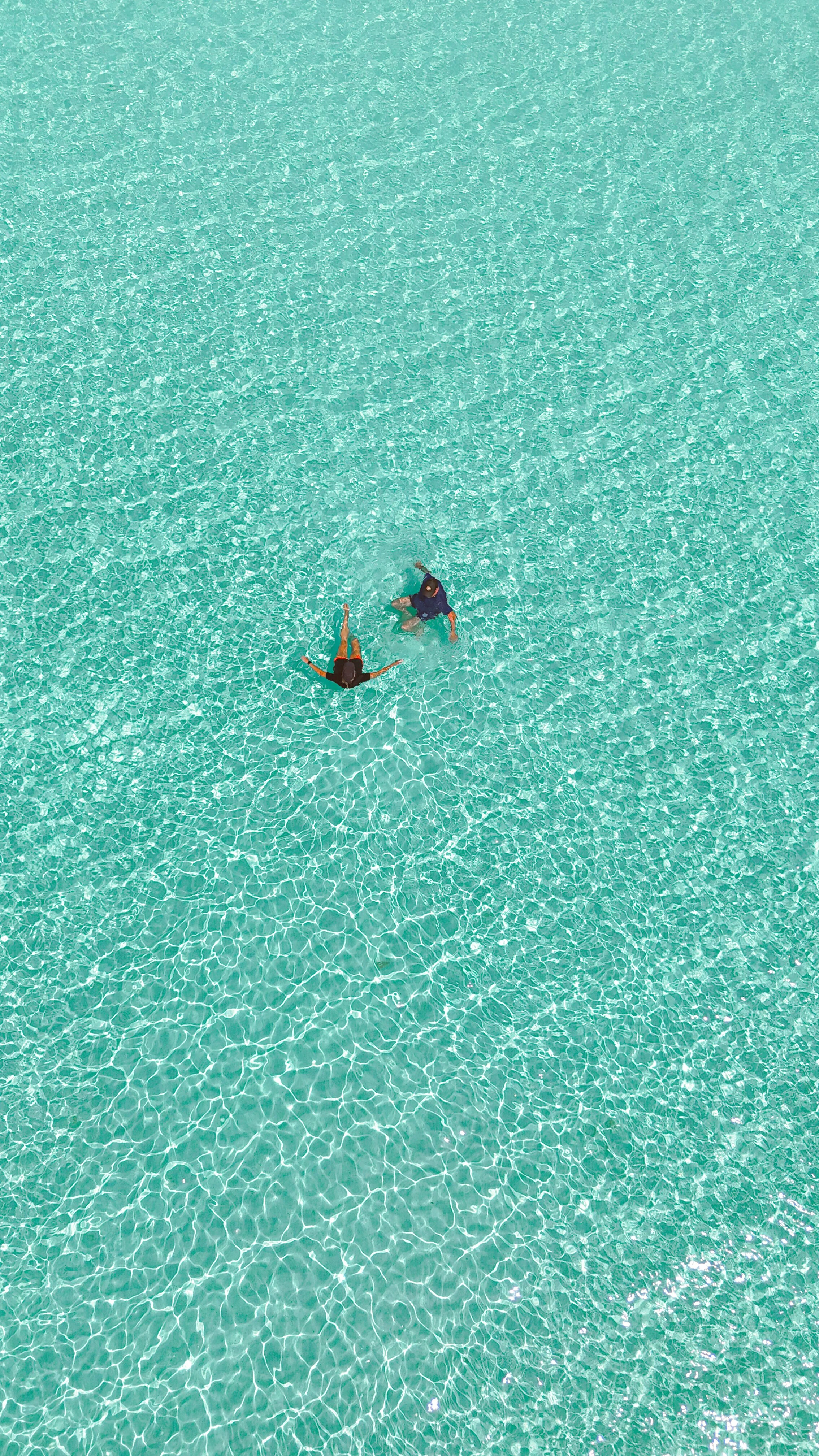 Two people swimming in a clear, turquoise ocean with visible ripples on the waters near K. Guraidhoo island.