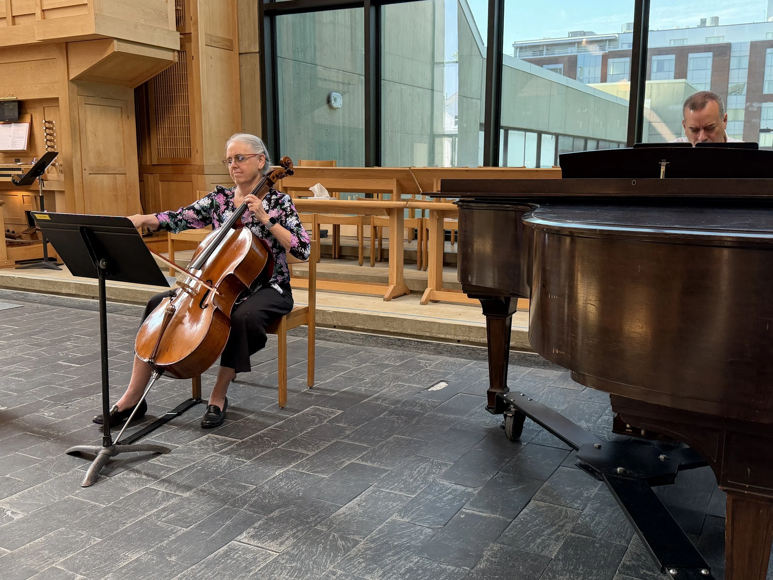 A woman playing a cello in Vermont in collaboration with a man playing a grand piano performing in a modern room. Cello music.