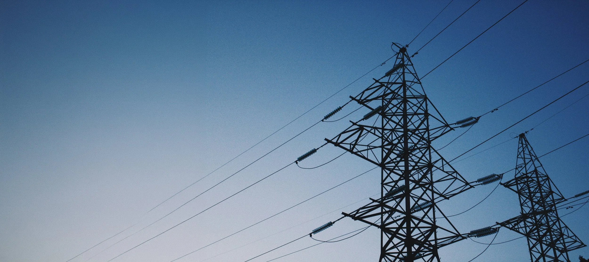 Silhouette of electrical transmission towers against a twilight sky.