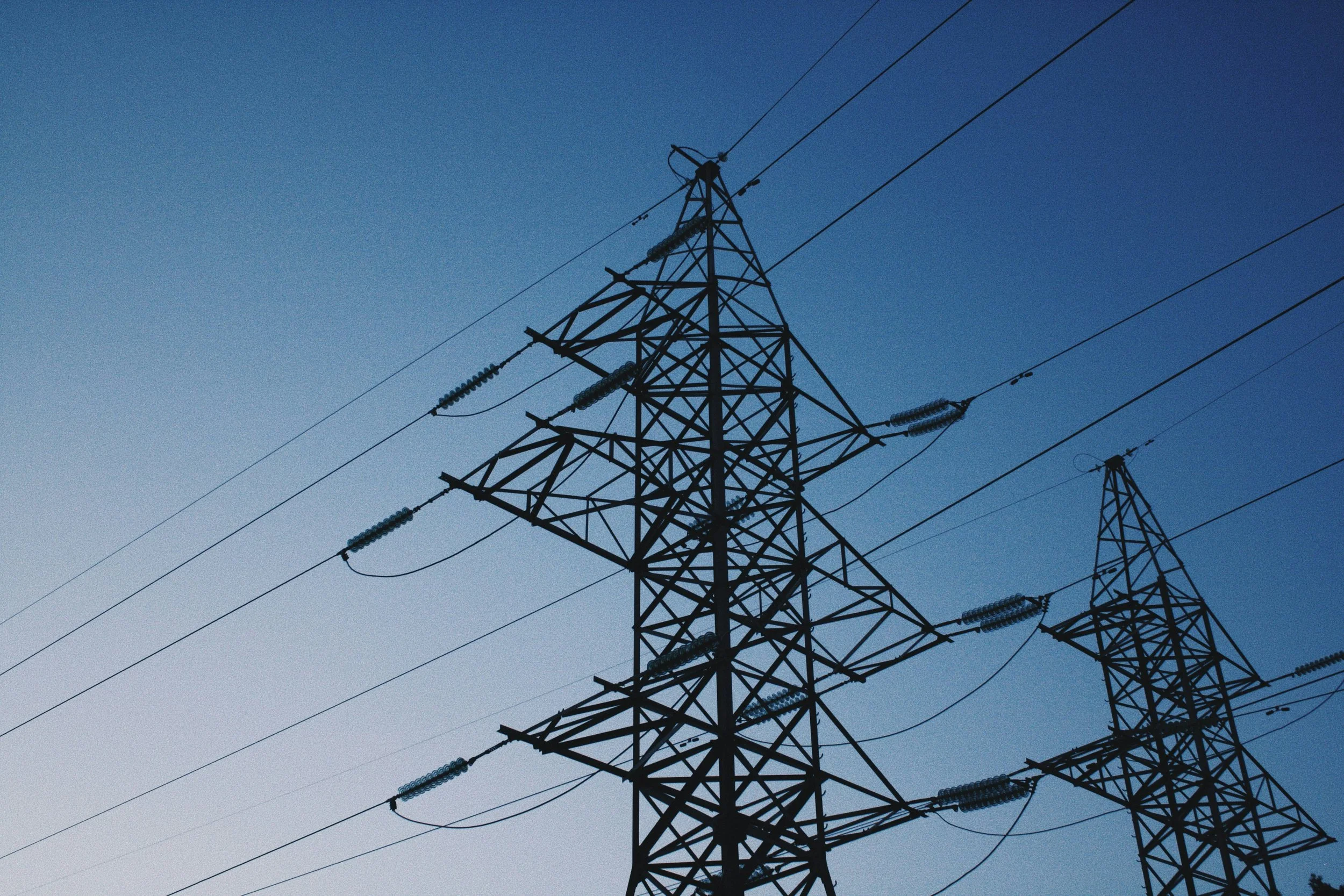 A close-up view of electrical power lines and transmission towers against a clear blue sky at dusk.