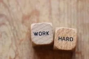 Wooden blocks with the words 'WORK' and 'HARD' on them, placed on a wooden surface.