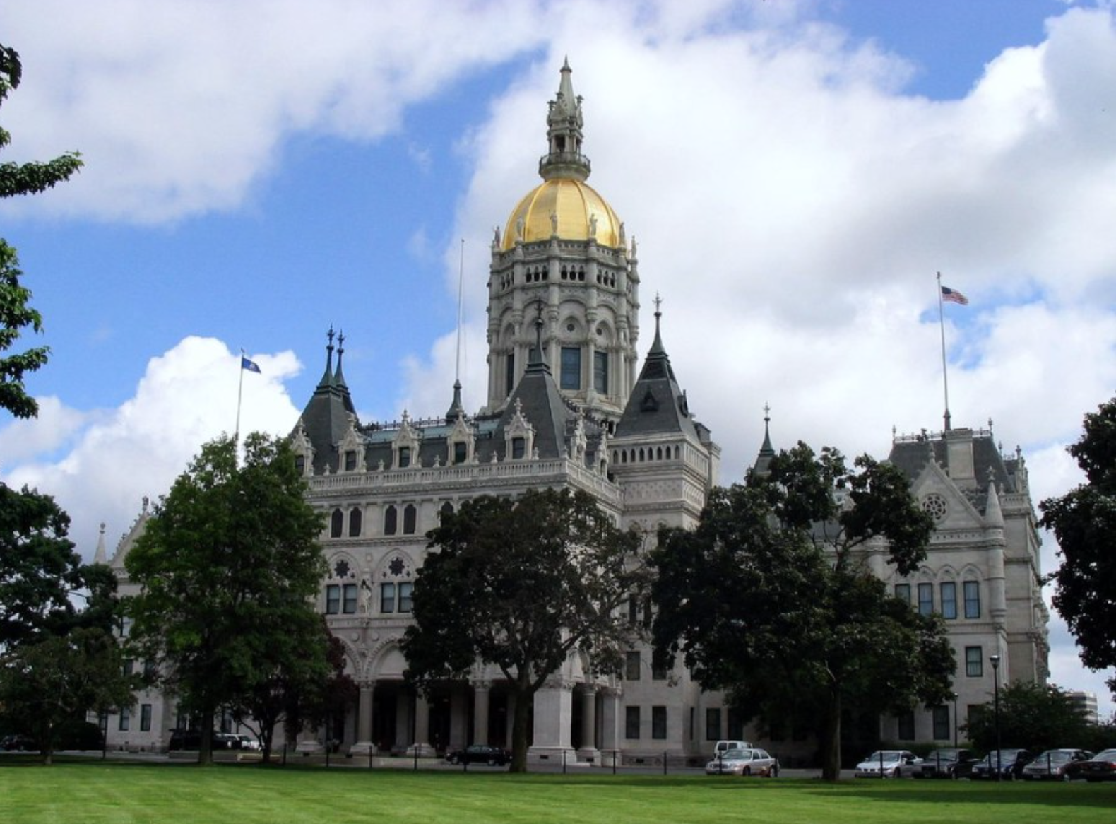 The historic California State Capitol building with a gold dome, surrounded by trees, under a partly cloudy sky.