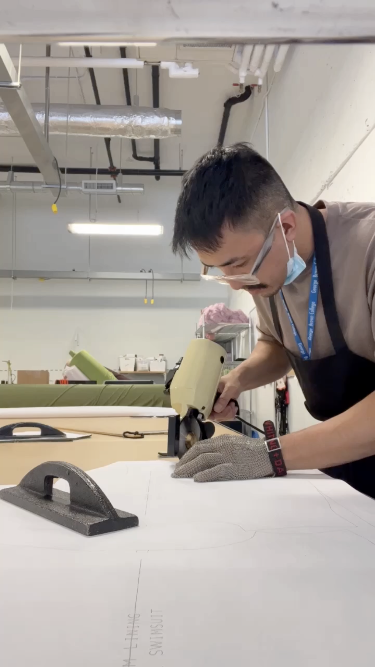 Carlos cutting garments on a production scale using an electric rotary cutter, a mesh safety glove, and pattern weights.