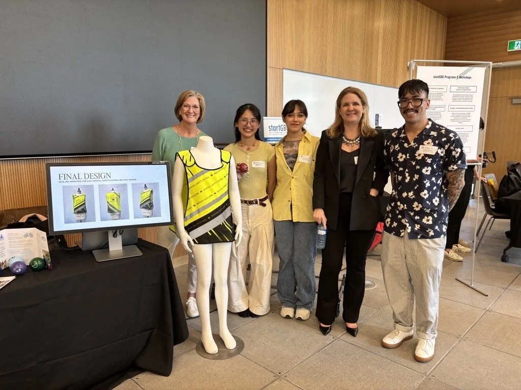 Carlos and his research team, standing beside a mannequin wearing a child's safety vest and a monitor displaying design images.