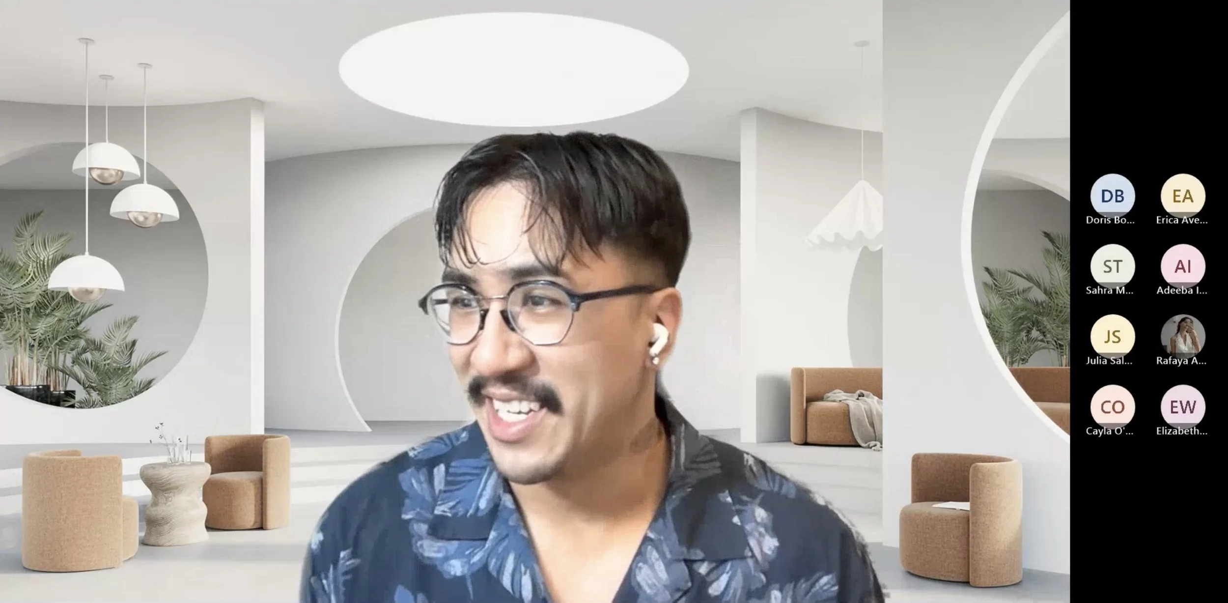 Carlos teaching in a virtual classroom, with a modern, minimalist background featuring circular cutouts, plants, and beige furniture.
