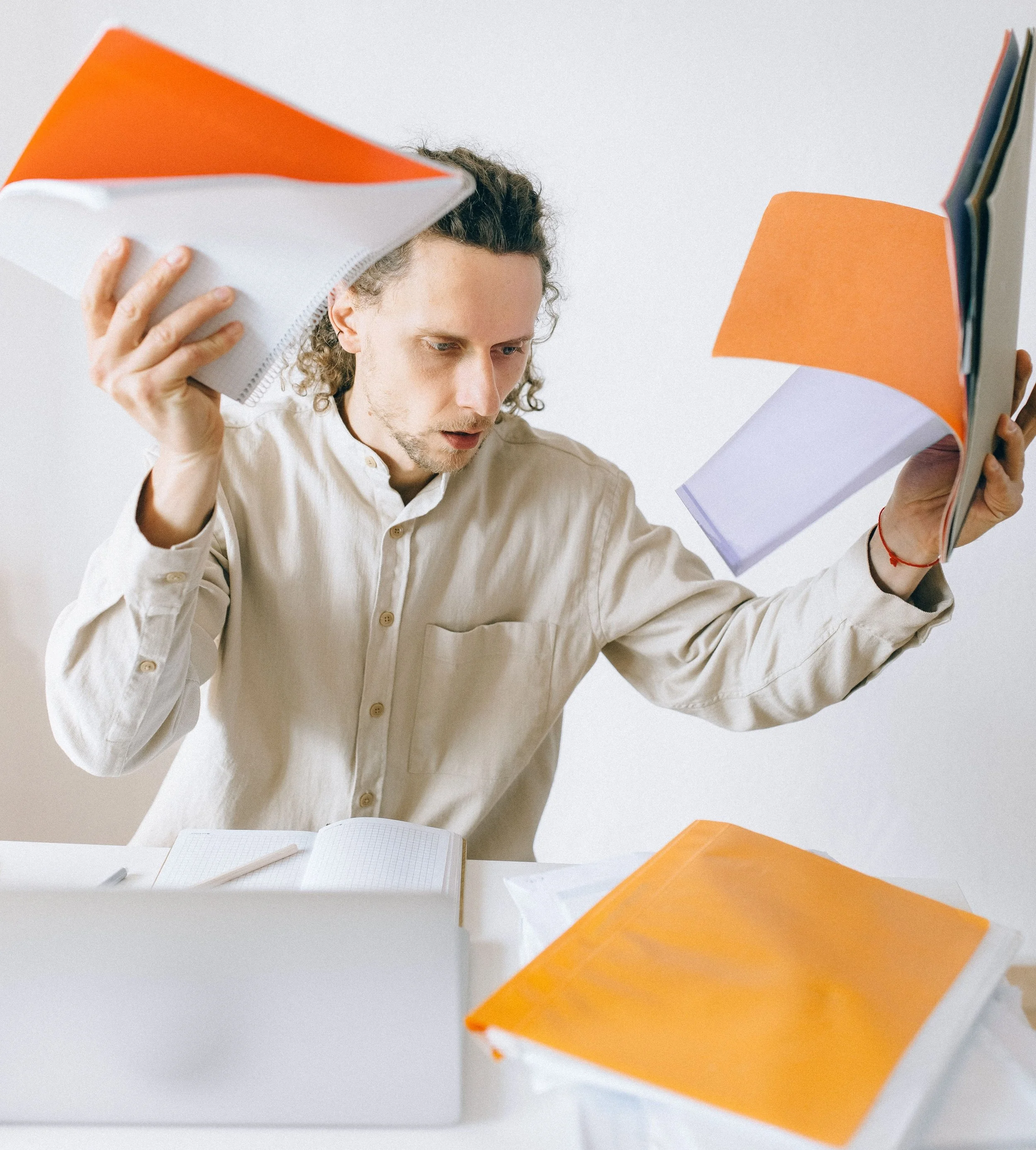 Un hombre sosteniendo varias hojas de papel de colores, con una laptop abierta en una mesa blanca.