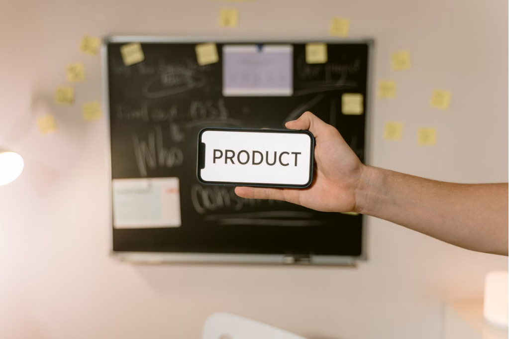 Una computadora portátil con gráficos y datos en la pantalla, una mano usando una calculadora, un teléfono móvil con gráficos, una lupa, y una taza de café en un escritorio blanco.