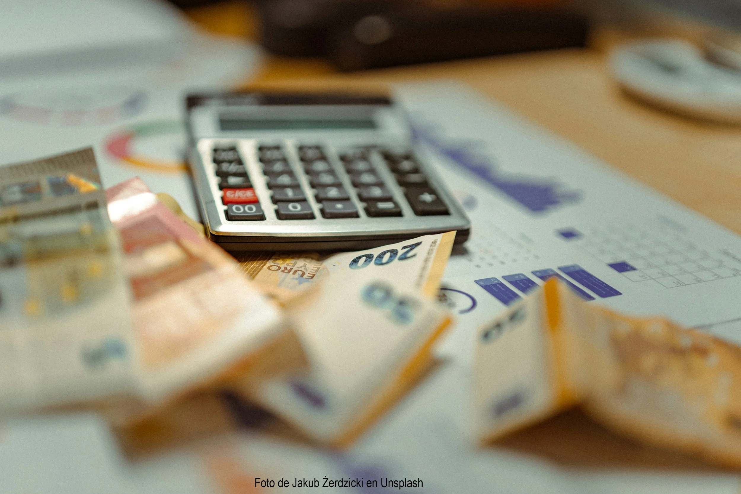 Calculadora sobre dinero en billetes de 200, con papeles y objetos diversos en un escritorio.