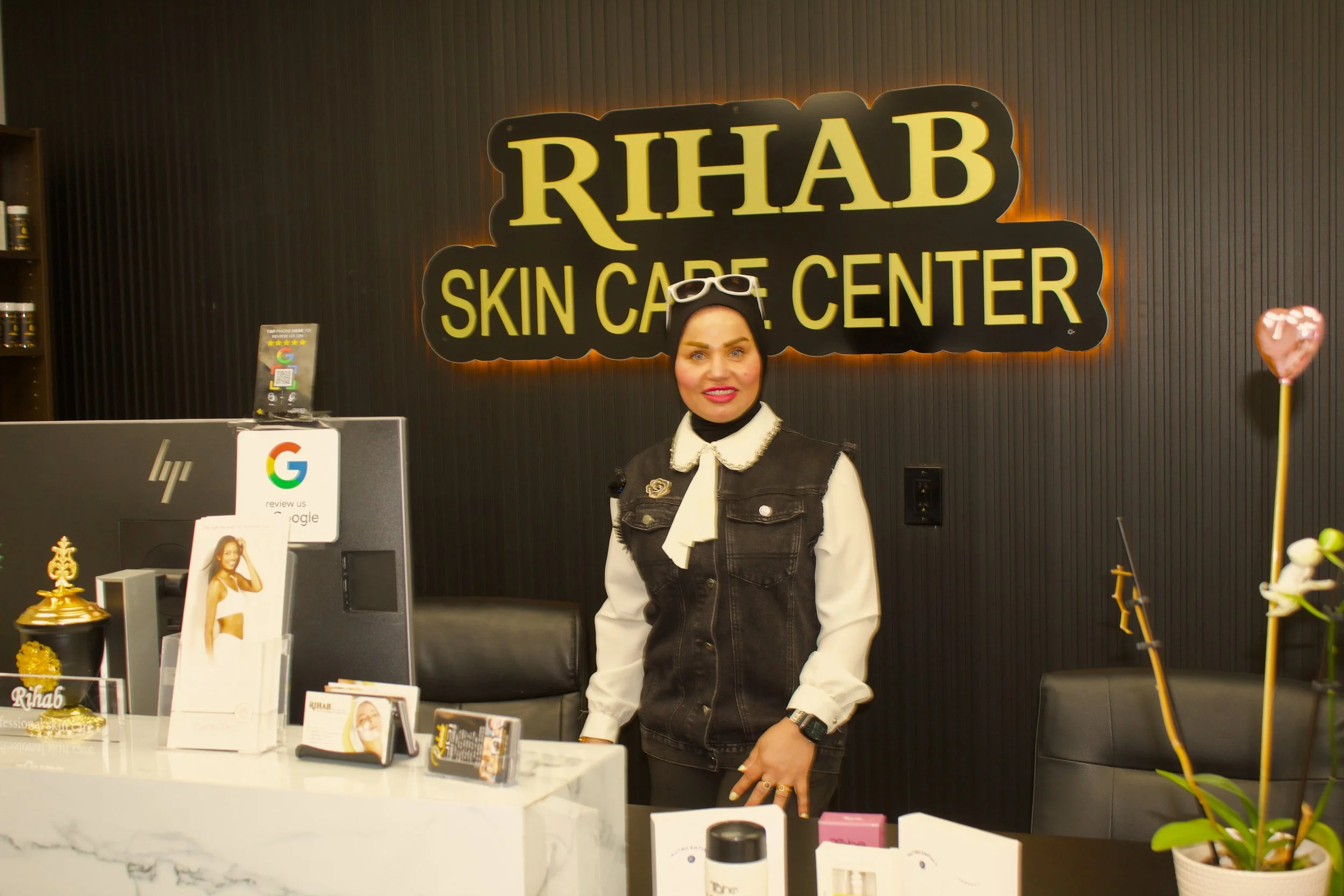 Reception desk at RIHAB Skin Care Center with a woman standing behind it, surrounded by skincare products and promotional materials.