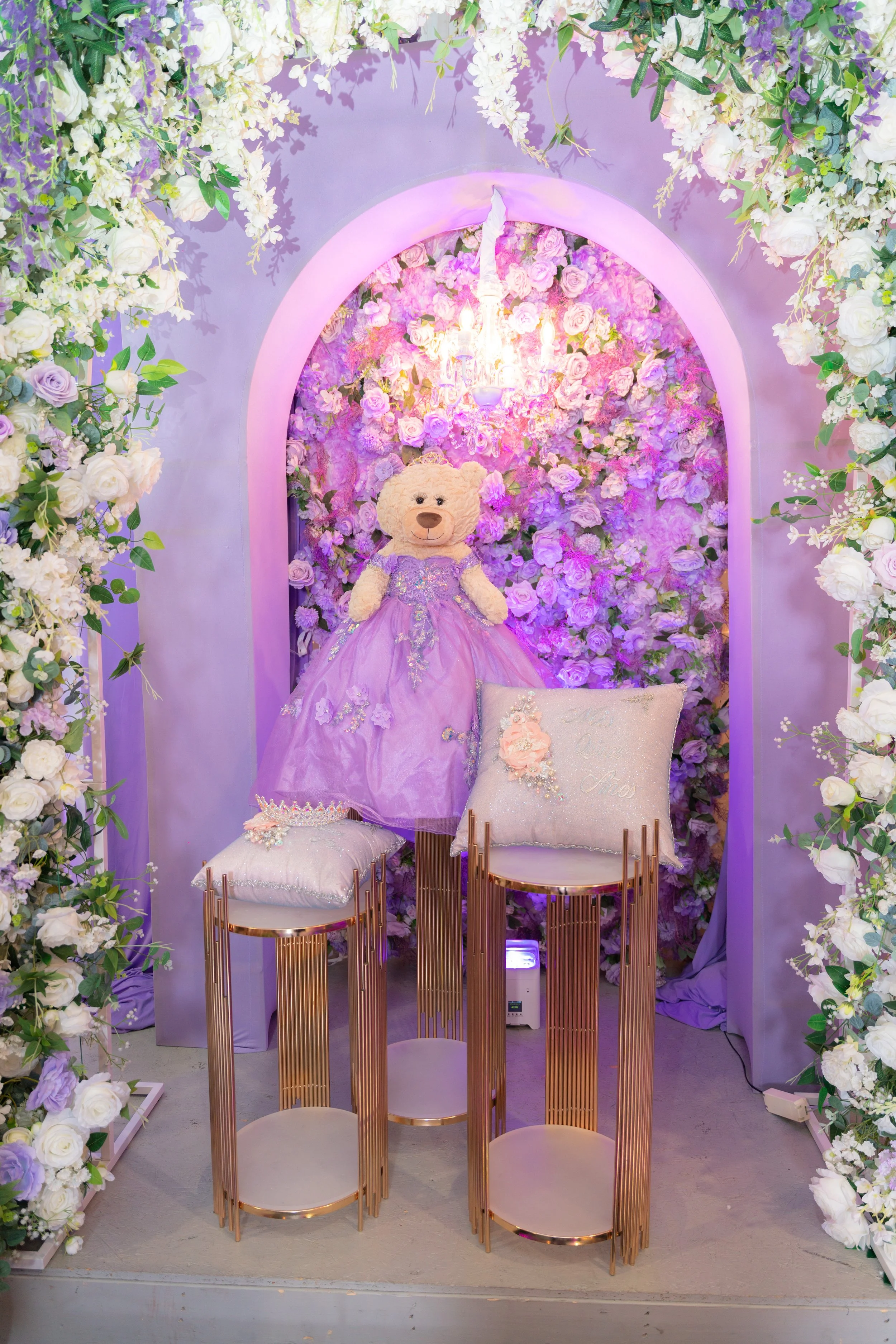 A bear with a purple gown on and pillows.