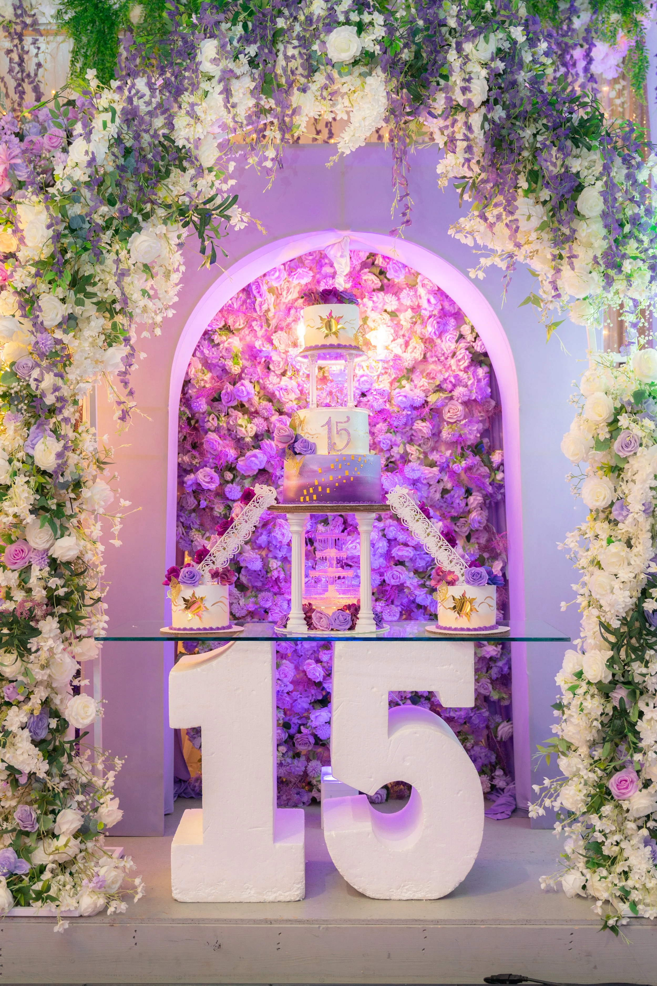 A cake that is purple themed on a table with the numbers 15.