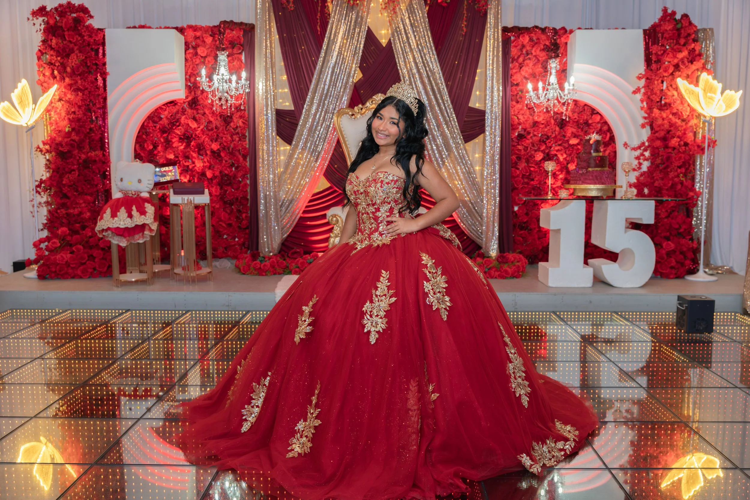 Birthday girl in red gown smiling in front of her throne chair.