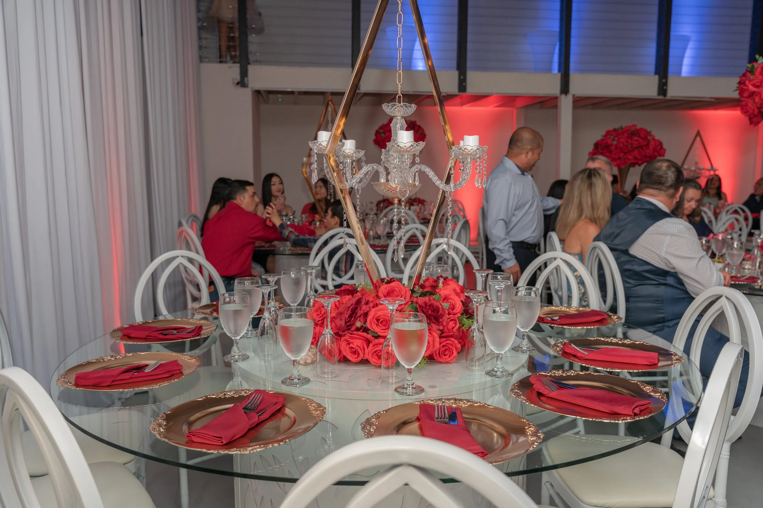 A fancy decorated table with red accent decorations, water, and roses.