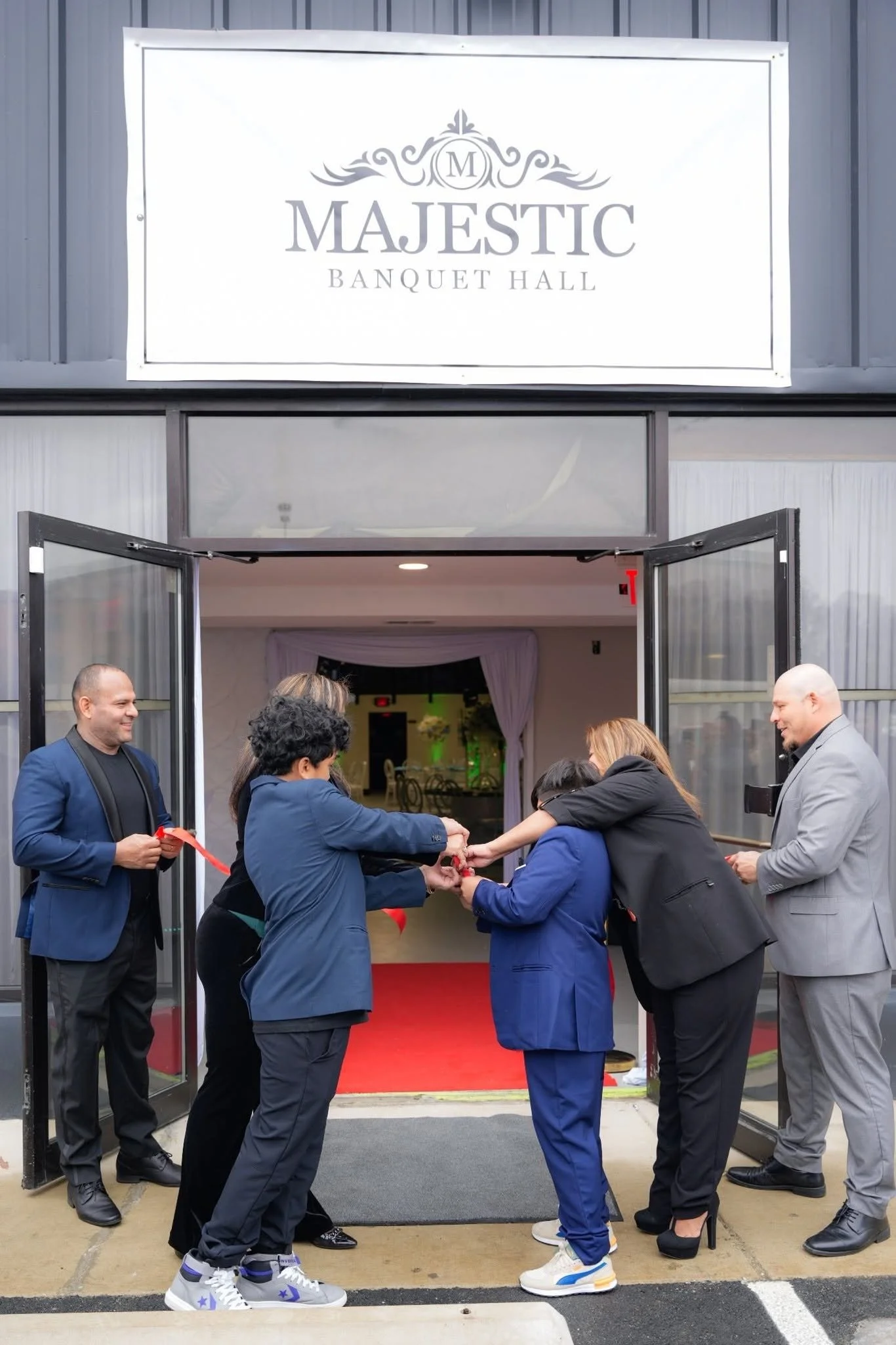 People attending an opening ceremony outside a banquet hall, with some holding a ribbon as part of a ribbon-cutting event. The door is open, revealing the interior of the hall.