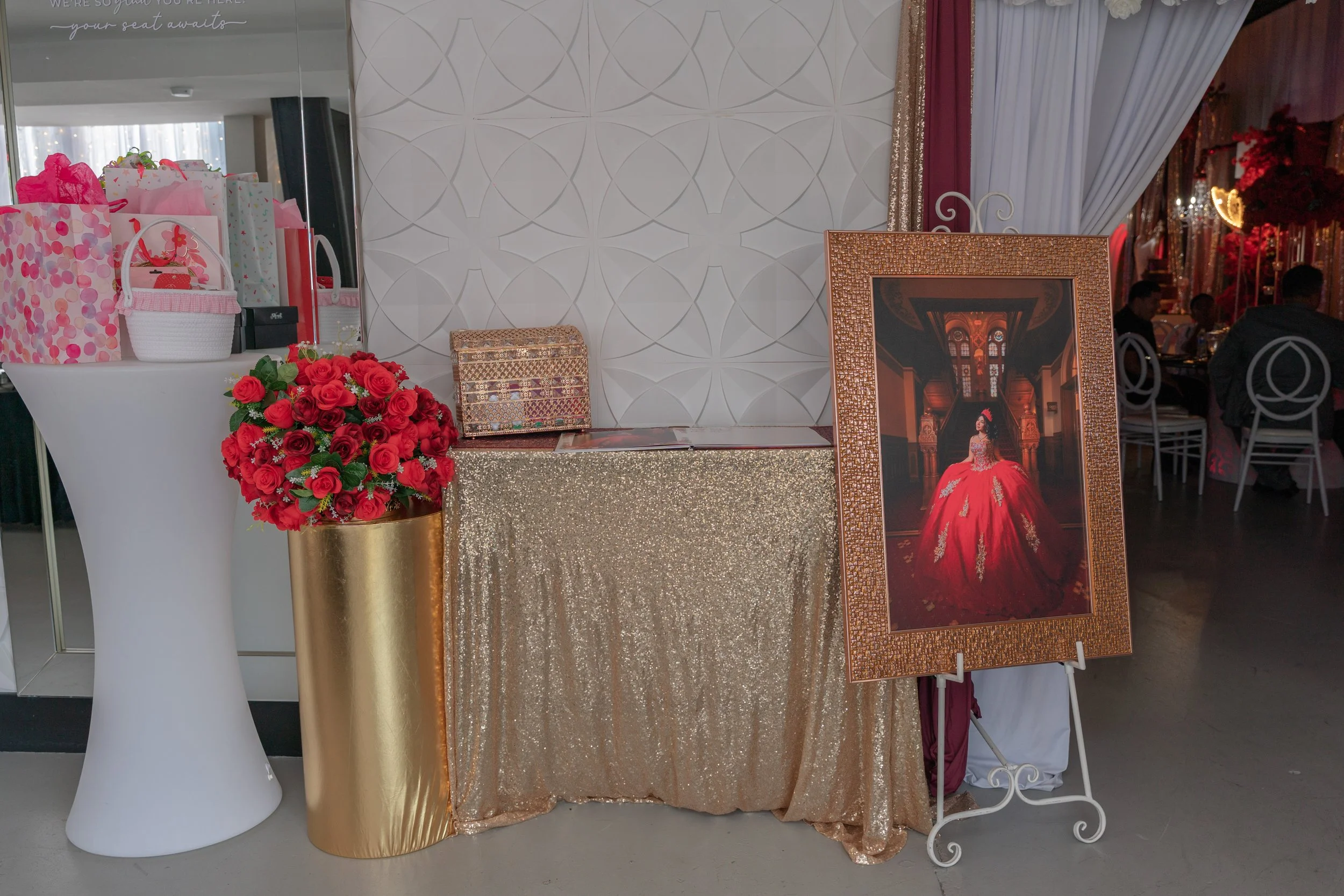 The entrance to a quince with a gifting area, roses, a guest book, and a photograph of a girl in a red gown.
