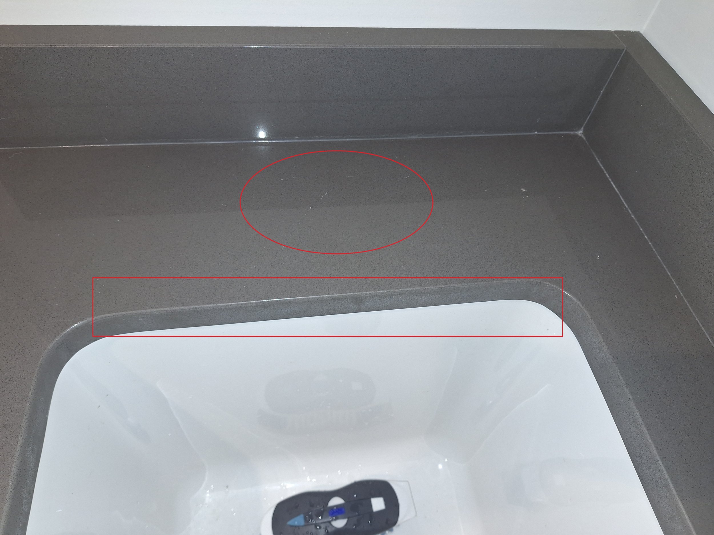 The image shows the inside of a washing machine with a dark-colored drum and a white interior. There is a small scratch or mark on the drum, highlighted by a red circle. The washing machine is empty, and part of the control panel is visible at the bottom of the image.