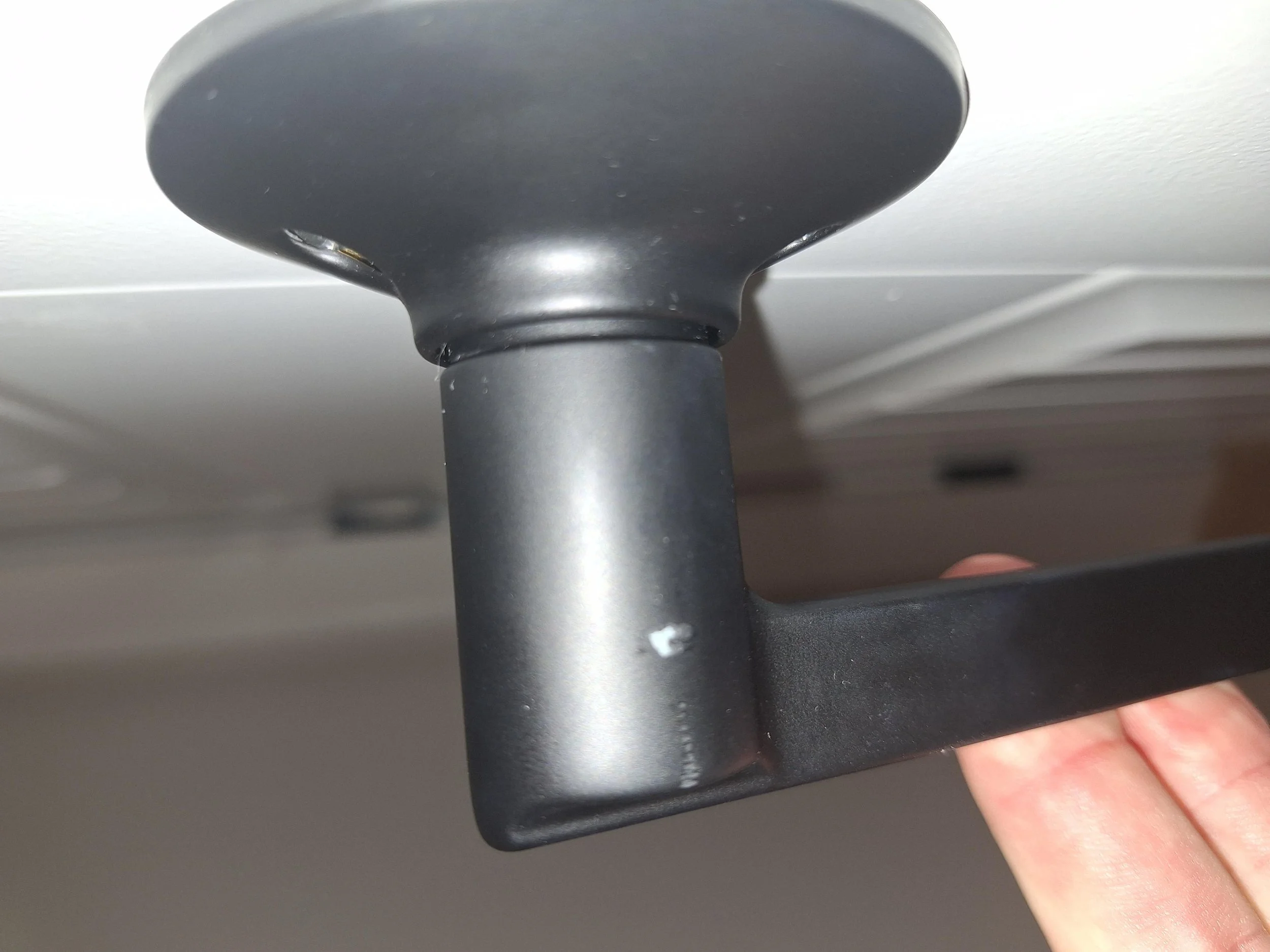 Close-up view of a black metal furniture leg with a person's finger pointing at it.