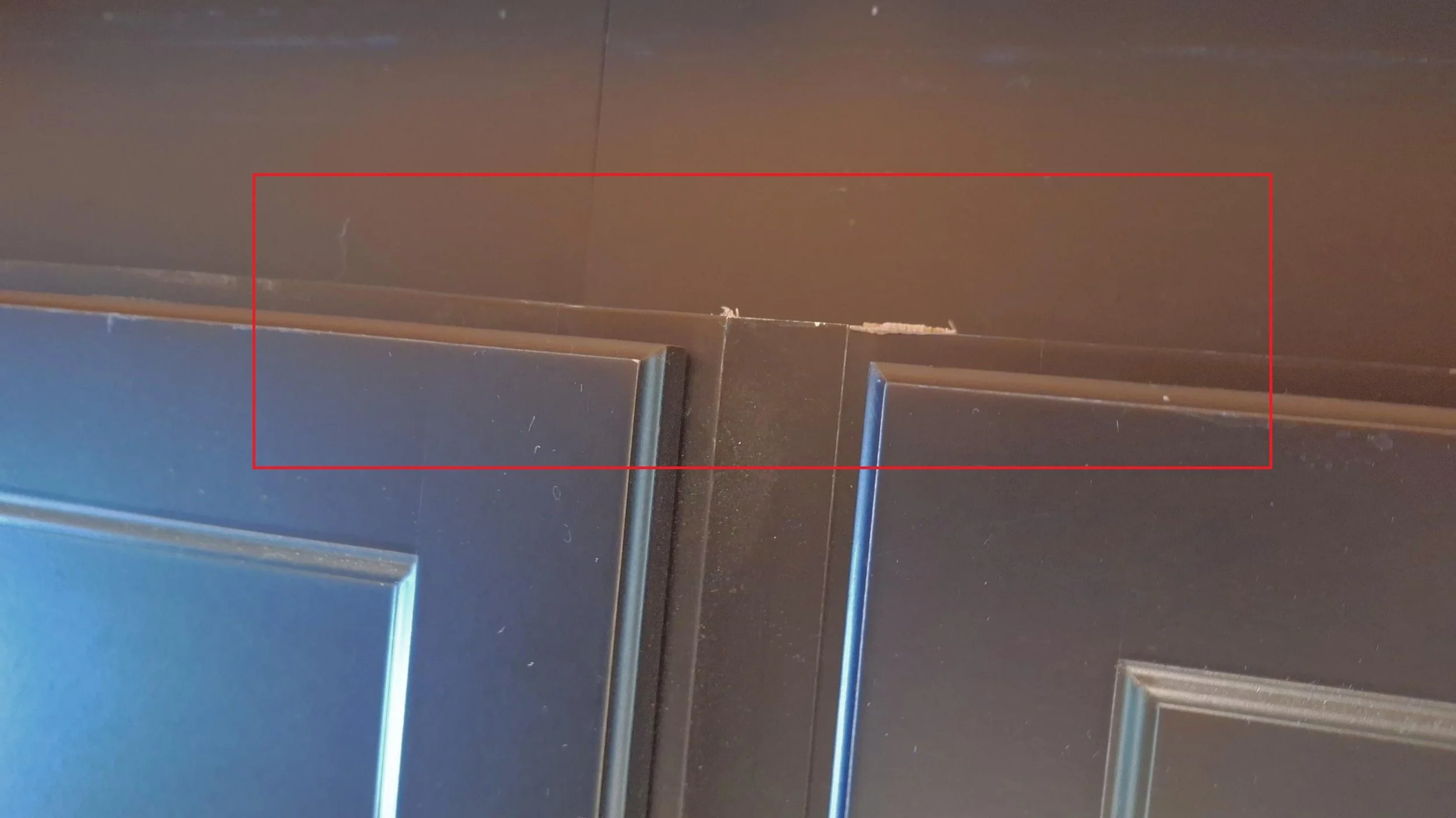 Close-up of a black kitchen cabinet with visible chipped paint and dust, with a red rectangle overlaying the image.