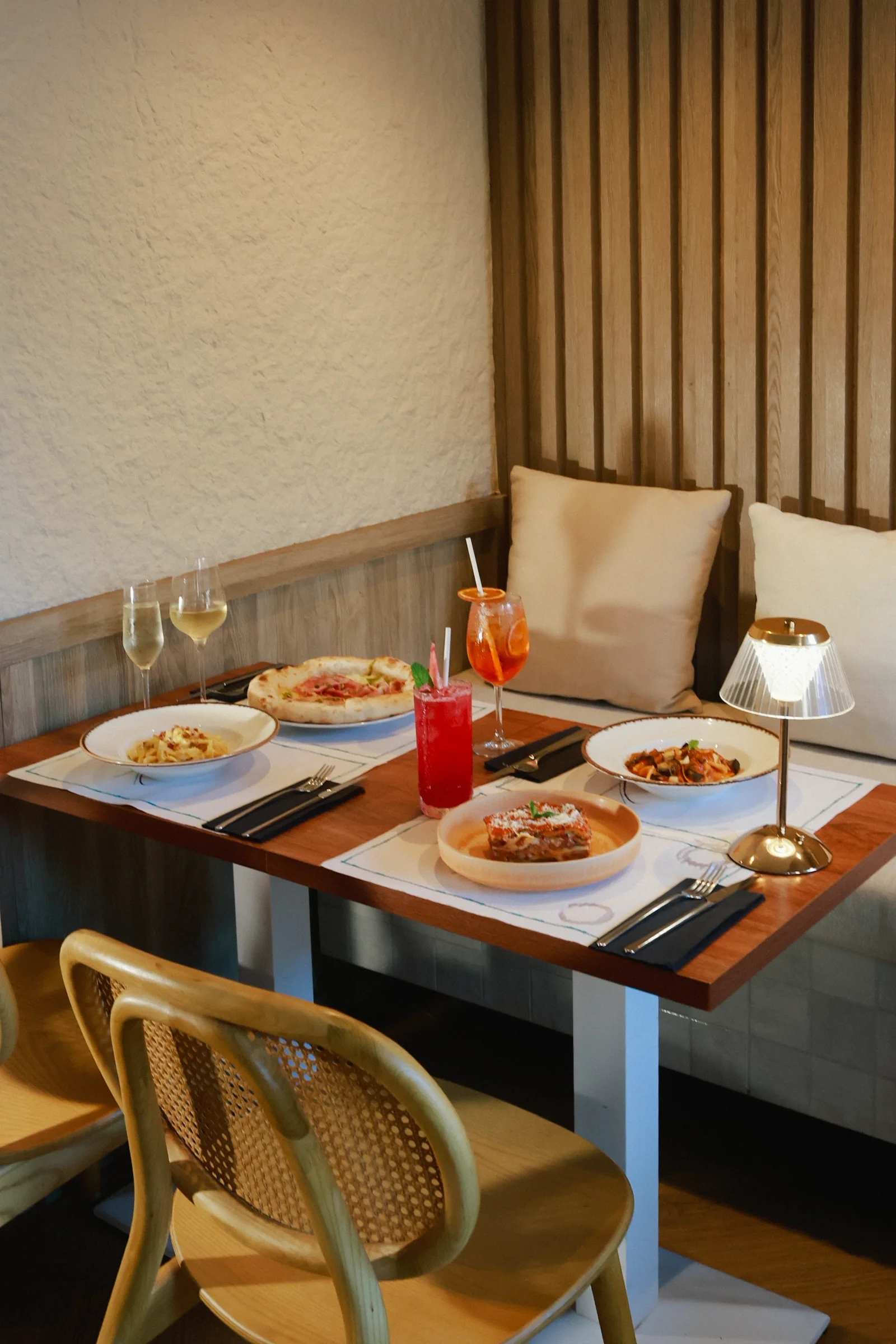 A banquette table at VERA in Porto set with Neapolitan pizza, lasagna, two pasta dishes, an Aperol spritz and white wine.