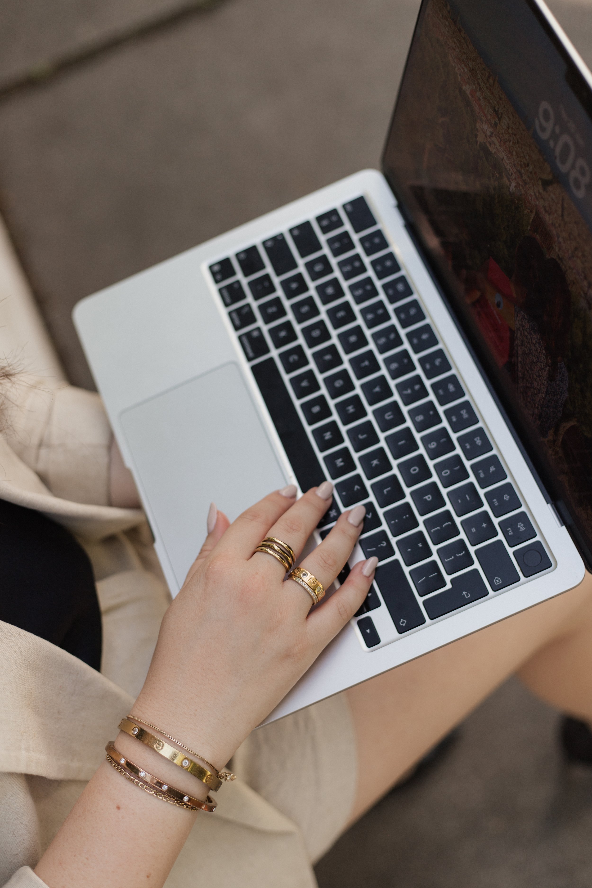 Nahaufnahme einer Hand mit mehreren Goldschmuckstücken, die auf einer Laptop-Tastatur liegt.