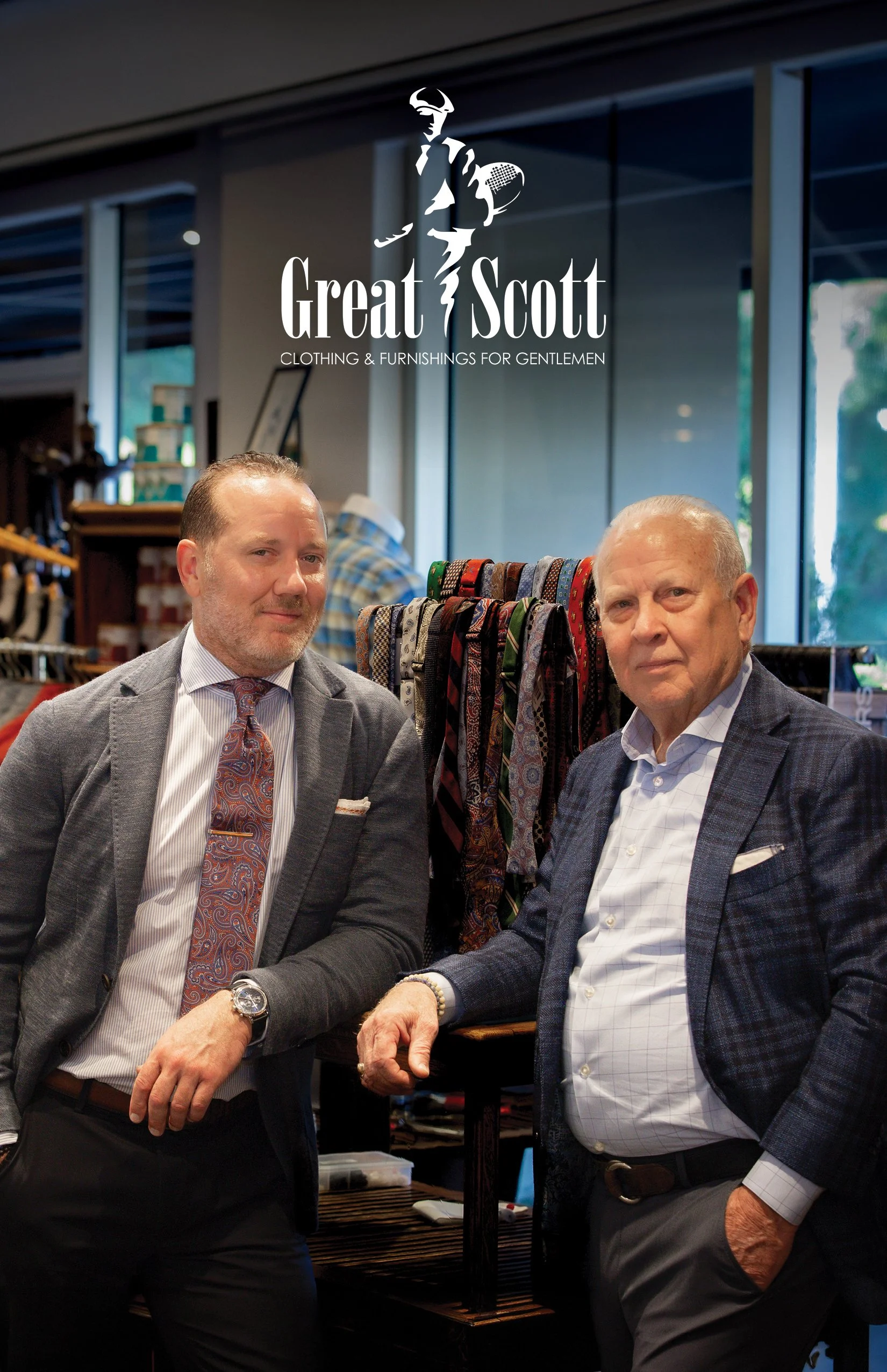 Two men in suits smiling and shaking hands inside a clothing store with racks of ties and suits in the background.