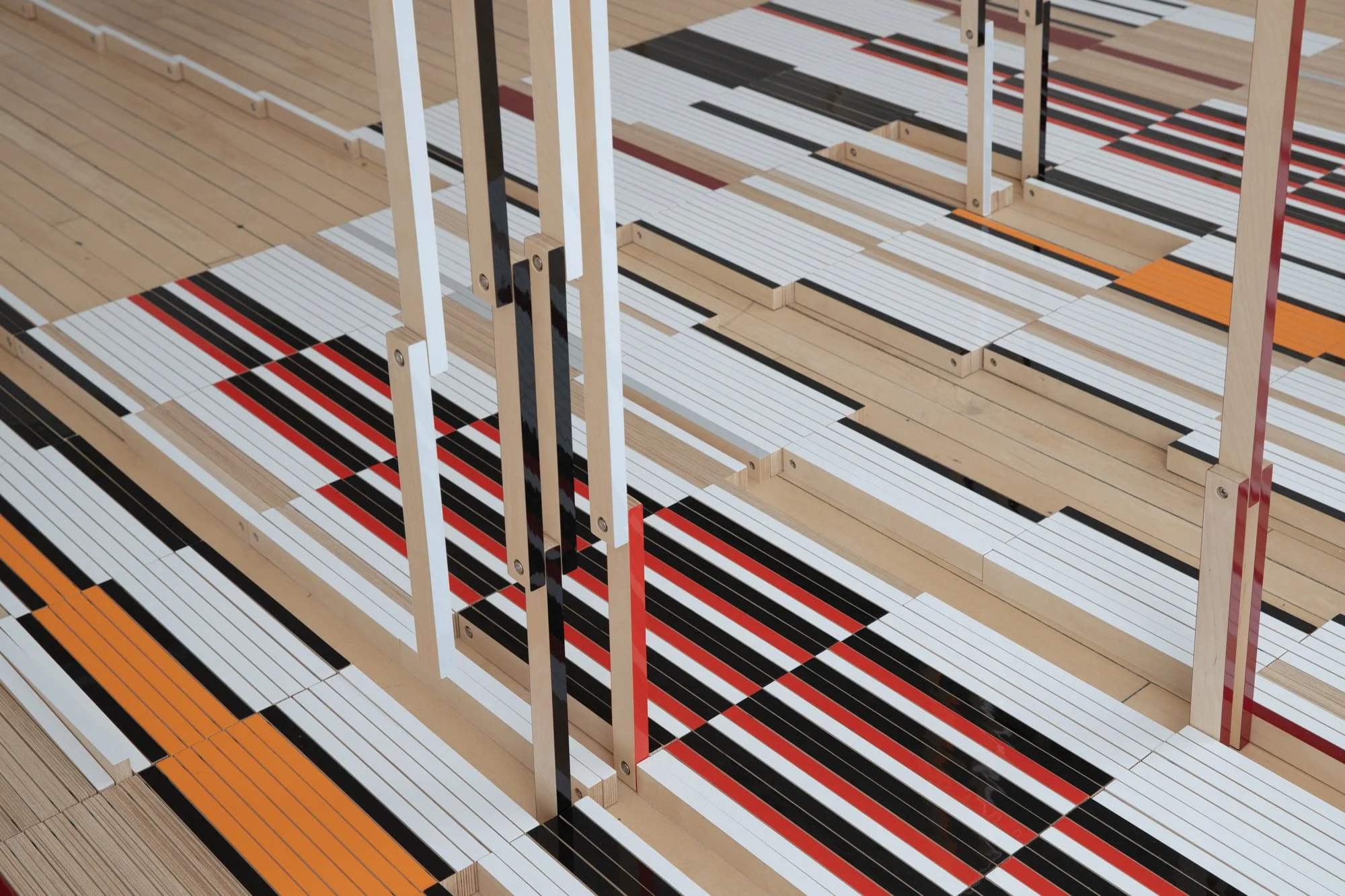 A modern art installation with geometric wood and colored lines on the floor, including black, white, red, and orange, with vertical wooden and metal supports.