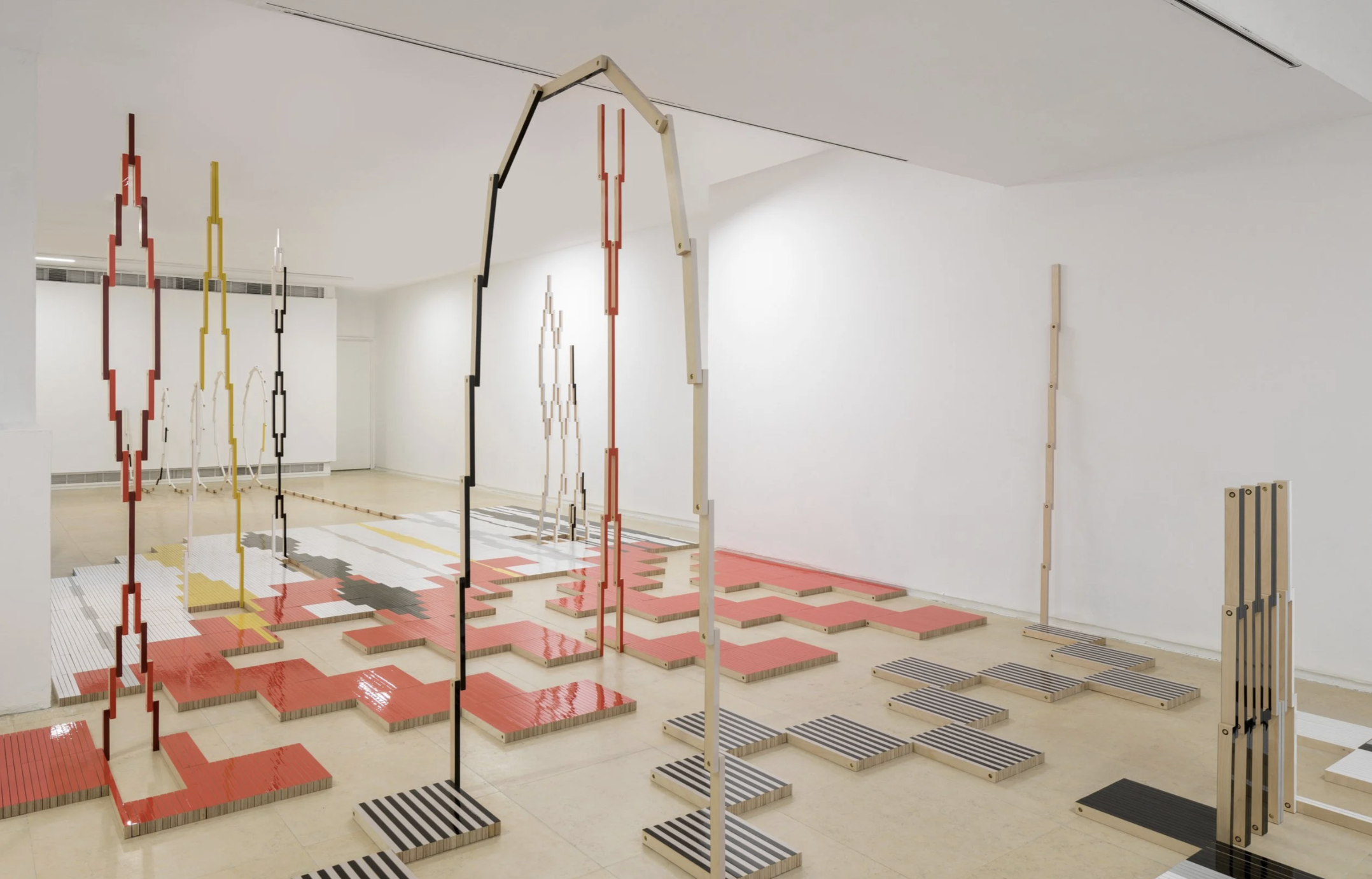 Interior of an art gallery featuring a modern installation with wooden and metal structures, colorful painted platforms, and geometric patterns on the floor.