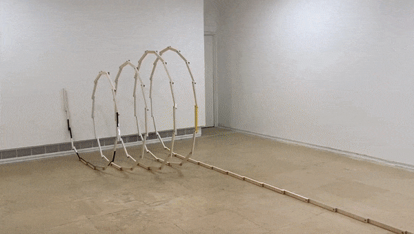 Three wooden hoops and a long wooden track set up in an empty room with white walls and a concrete floor.