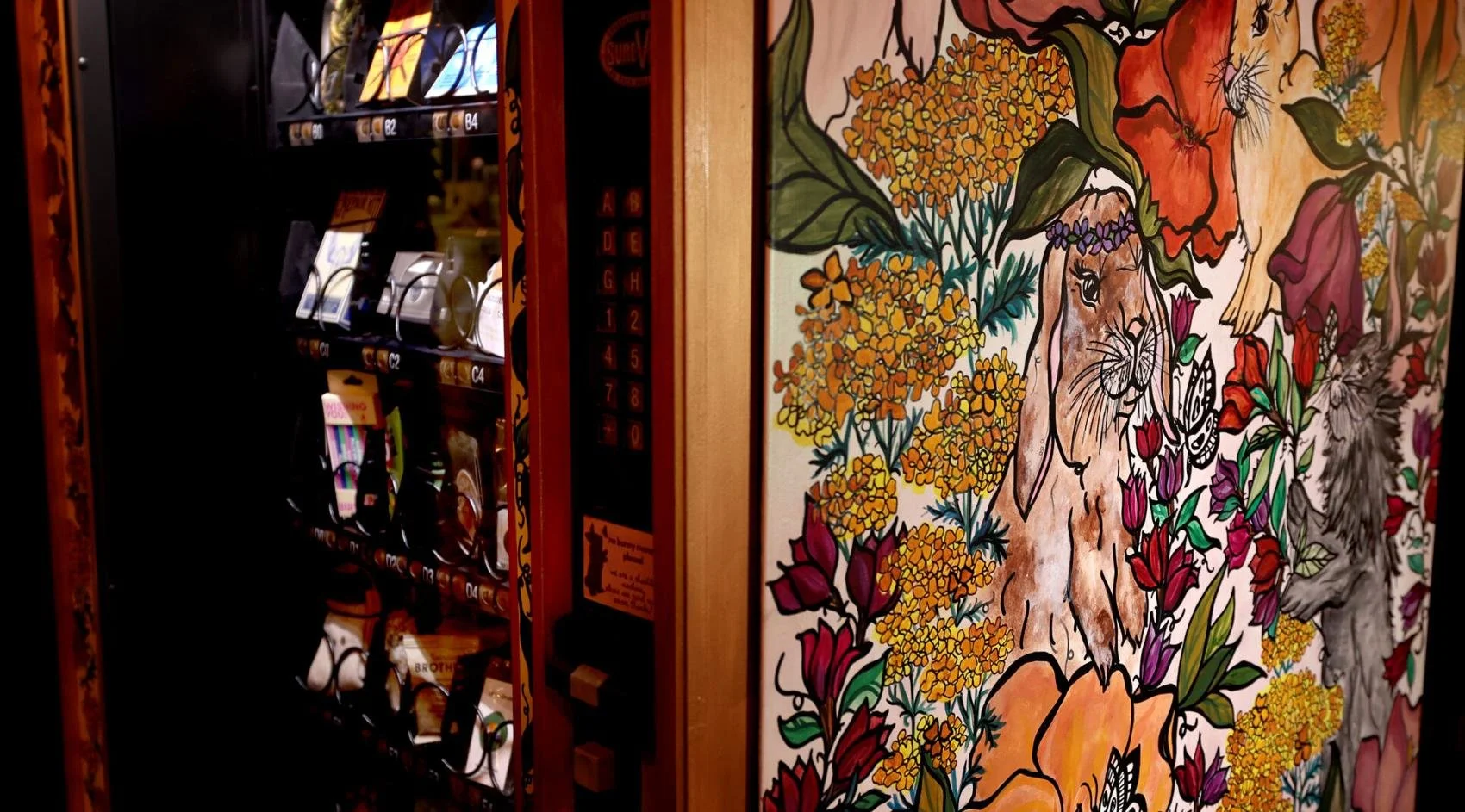 A wall with a colorful mural of wild animals and flowers next to a vending machine with snacks.