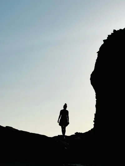Silhouette of woman walking under cliff
