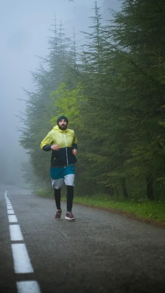 Man in windbreaker and hat jogging on path in fog