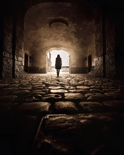 Fish eye perspective of woman walking through tunnel to open doorway of light