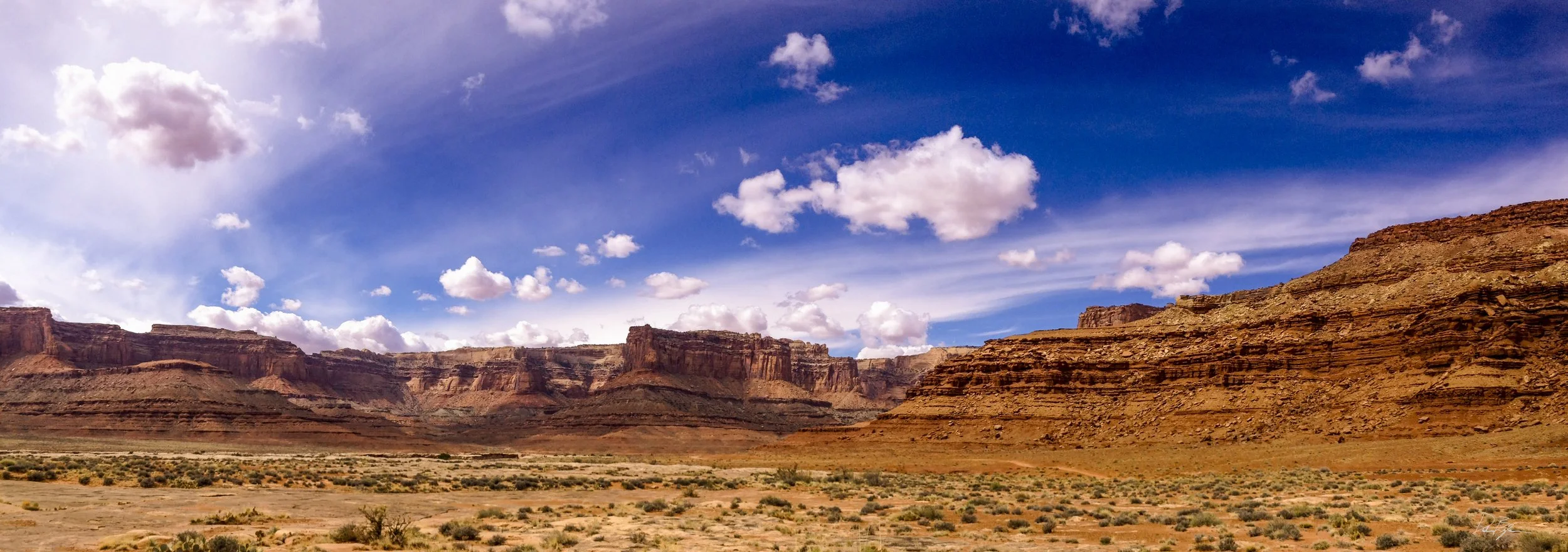 A desert landscape with large red rock formations under a blue sky with scattered white clouds.