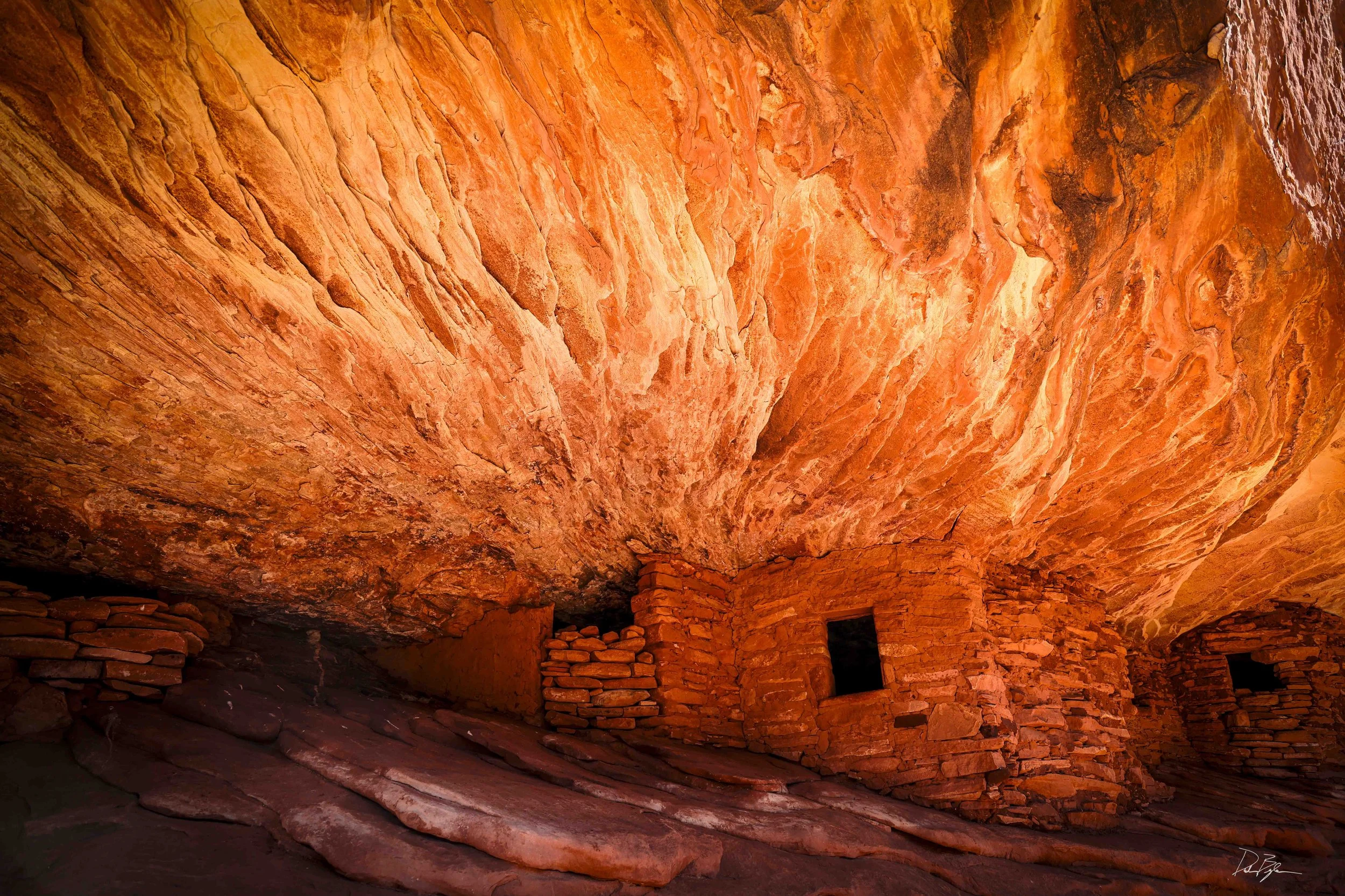 Inside a cavern with orange and red streaked rock formations on the ceiling and walls, and some stacked stones and small openings at the base.