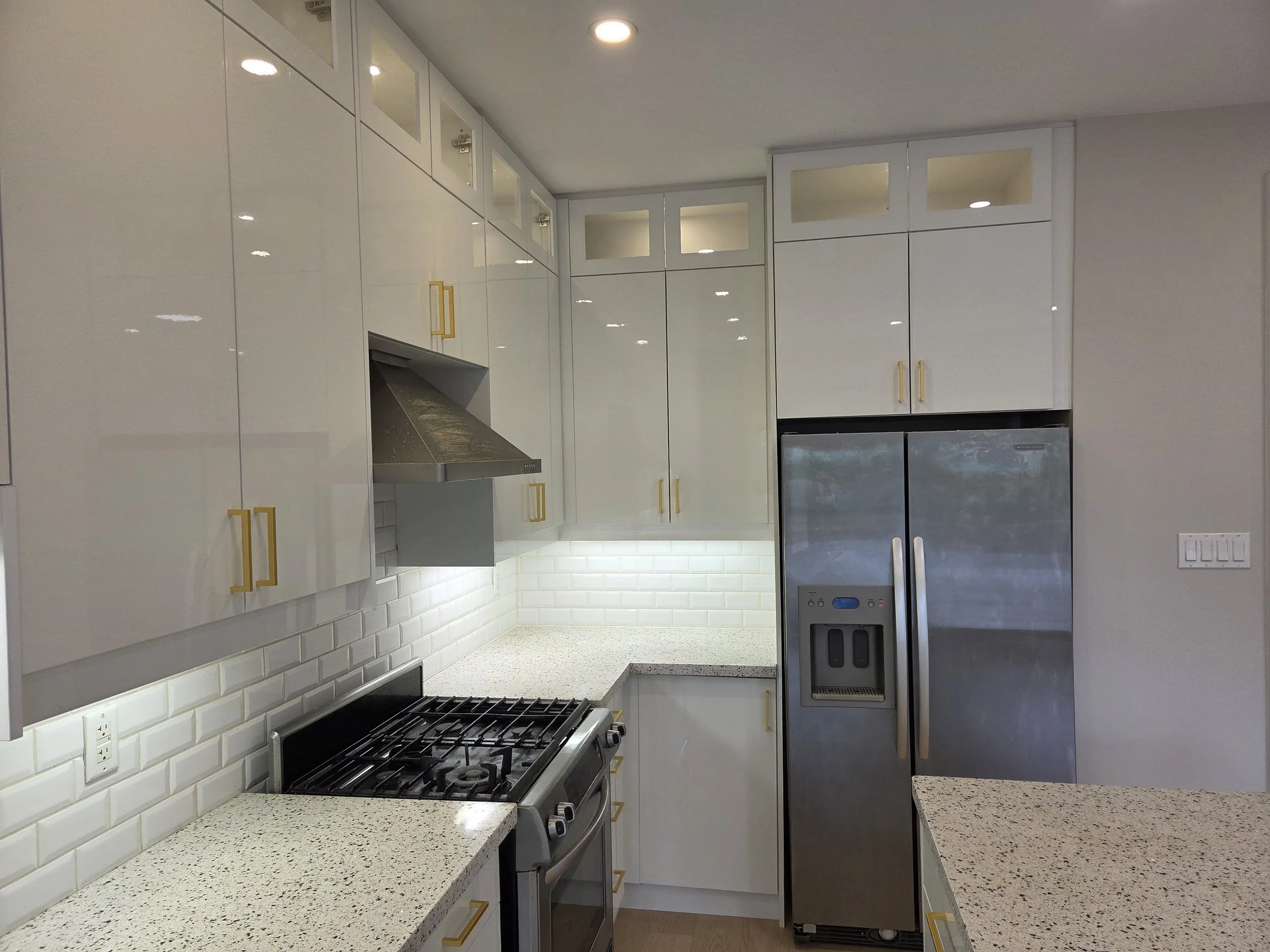 Modern kitchen with white cabinets, gold handles, a gas stove, a white subway tile backsplash, and stainless steel appliances.