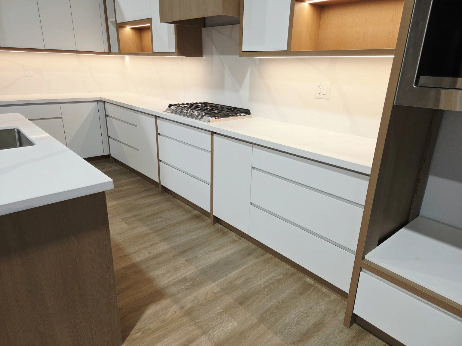 Modern kitchen with white cabinets, wooden accents, and a built-in gas stove on the countertop.