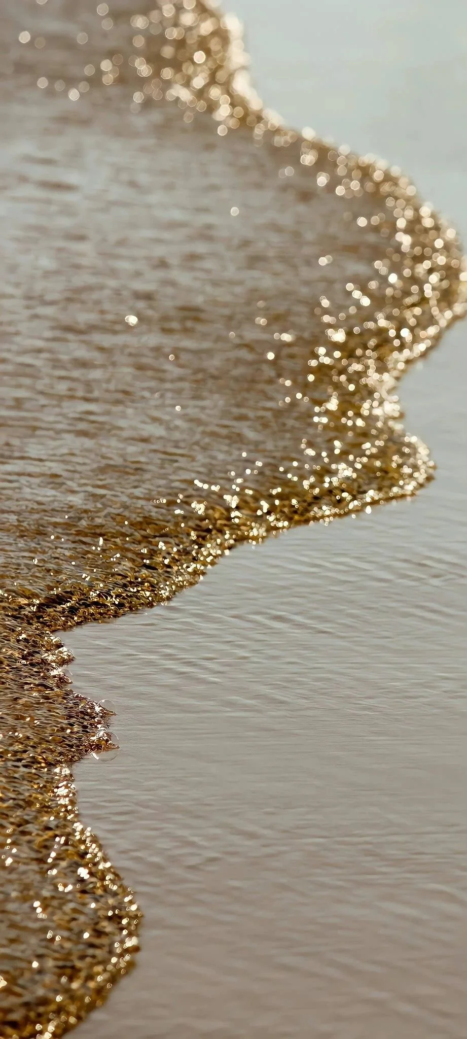 Close-up of wet sand on the beach with small waves washing over it, sparkling in the sunlight.