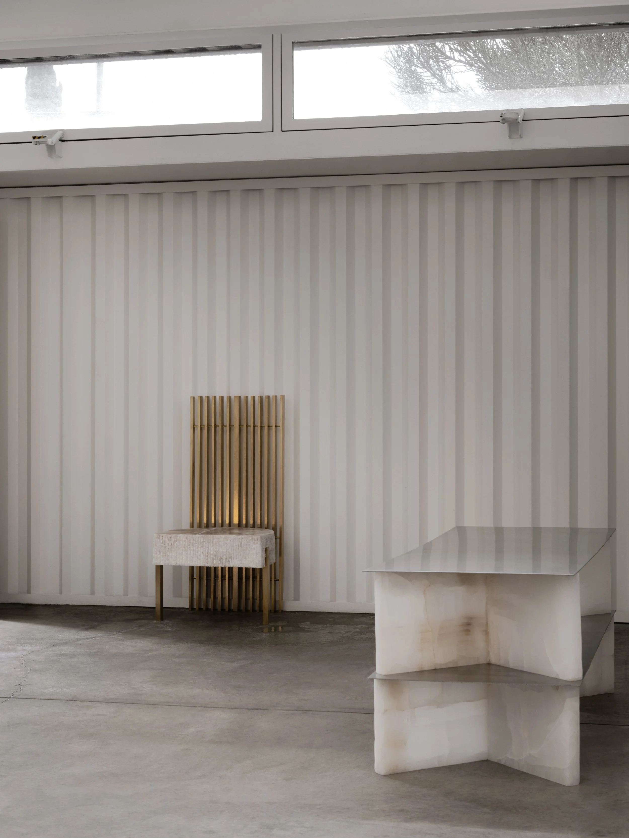 Minimalist interior with a marble table, a wooden slatted chair, and beige vertical striped wall panels.