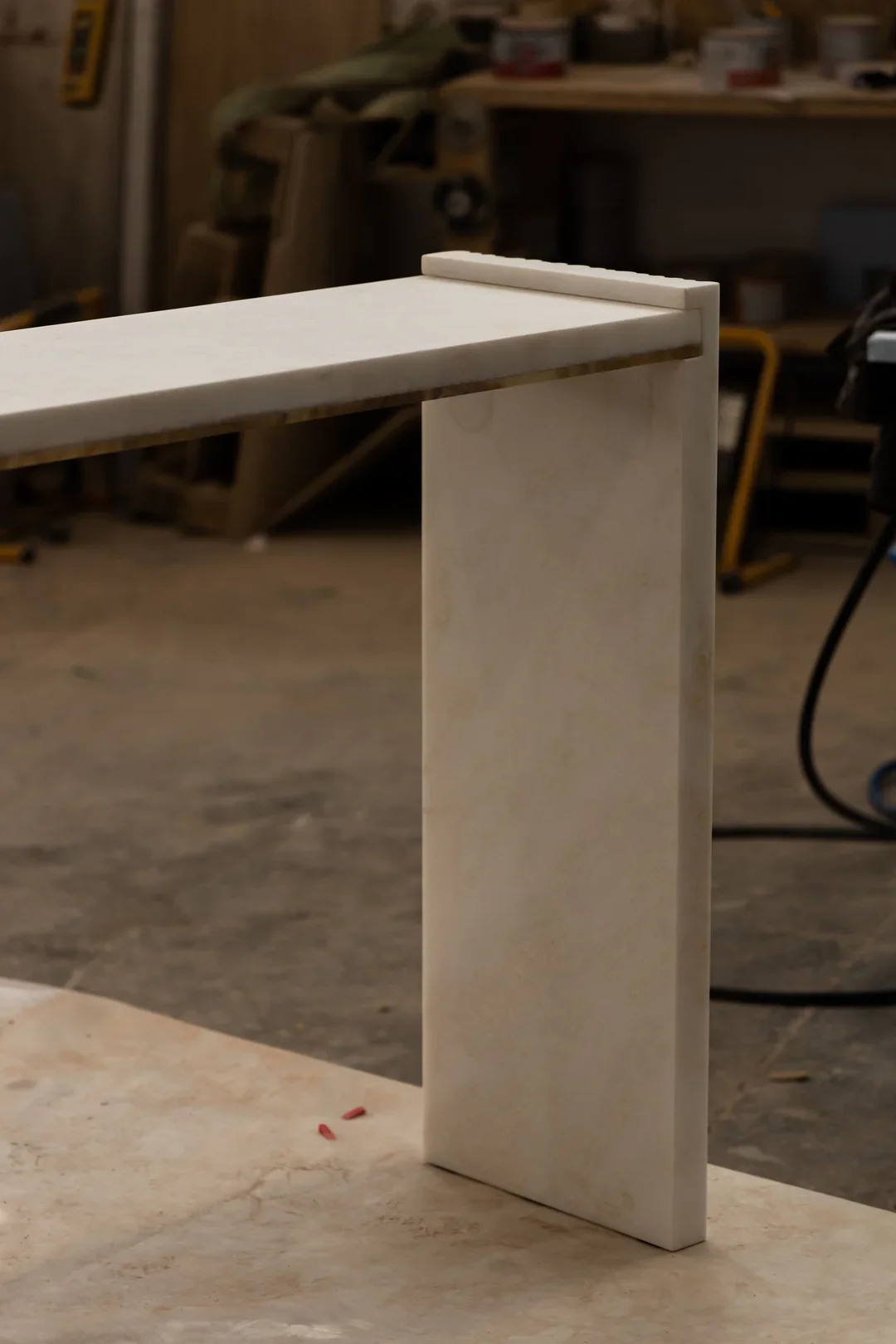 A piece of wood with a vertical support leaning against a worktable in a woodworking shop.