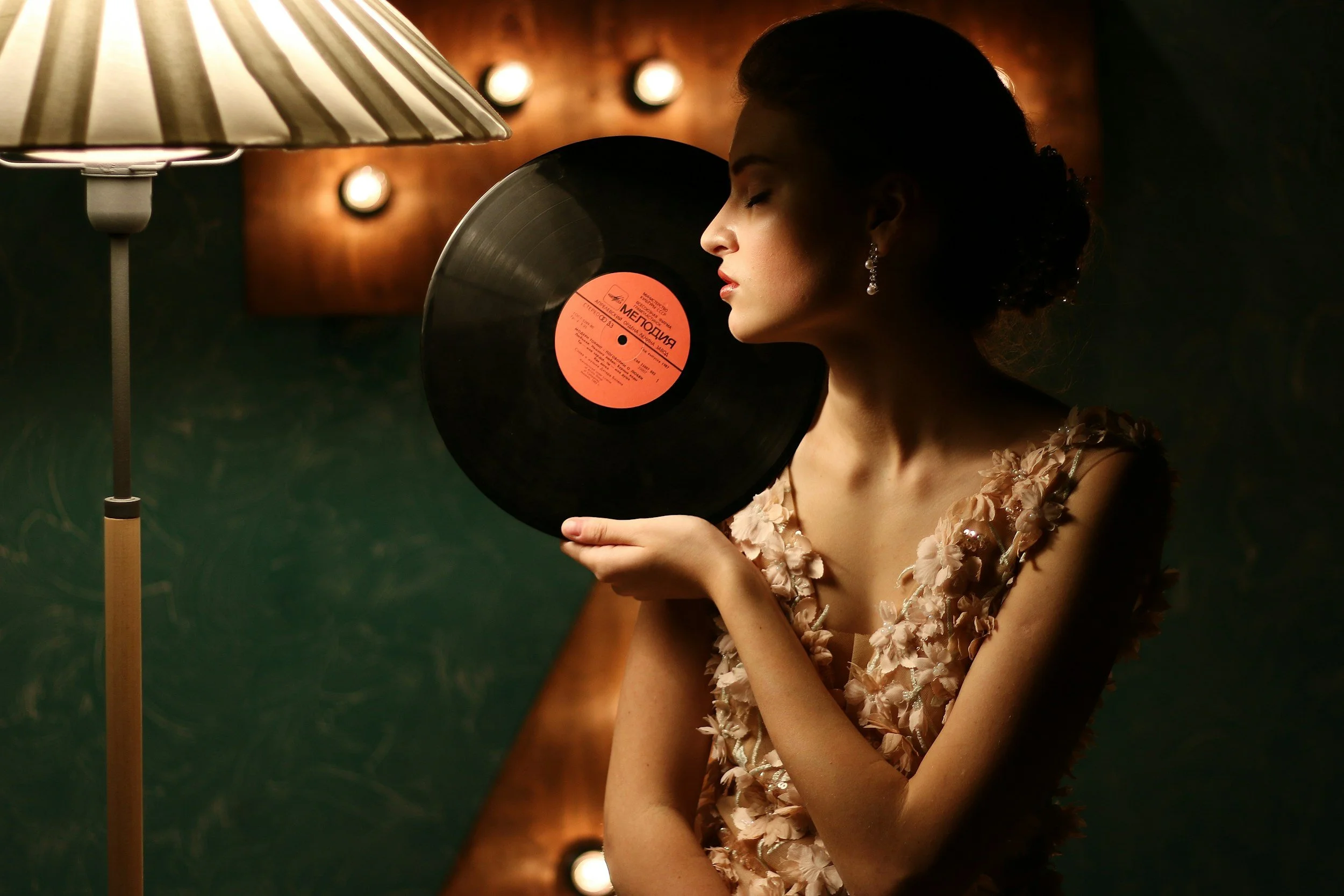 Une femme élégante tenant un disque vinyle devant un lampadaire dans une ambiance chaleureuse.