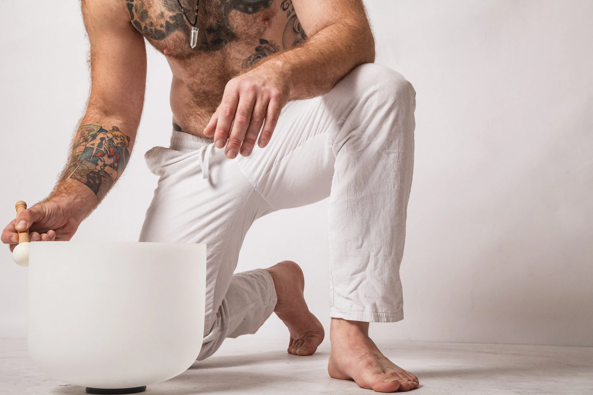 Person in white pants practicing yoga or meditation, kneeling with one hand on the floor and the other hand resting on the knee, against a plain white background.