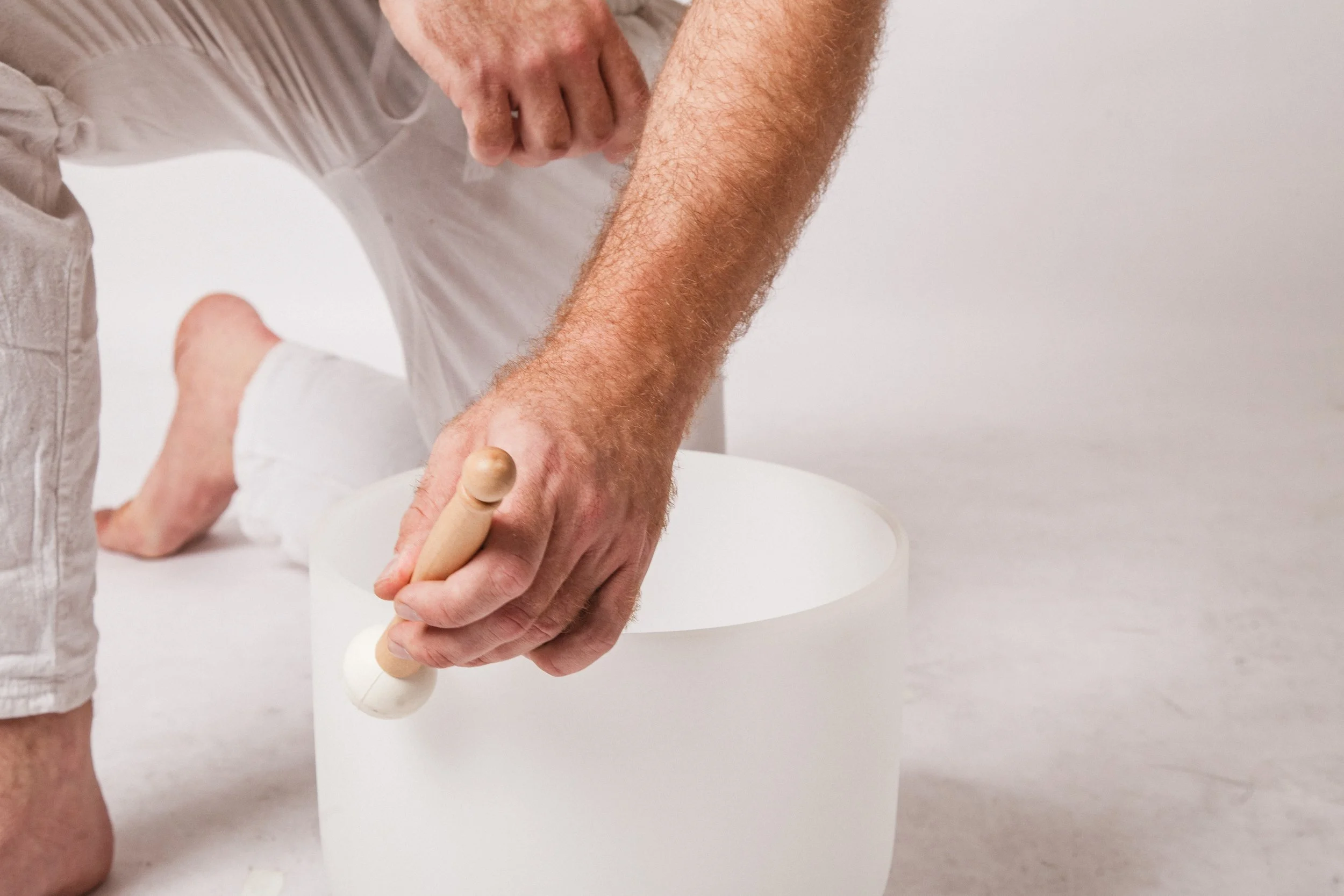 A person with hairy arm and white gloves shaping white clay with a wooden modeling tool on a white surface.
