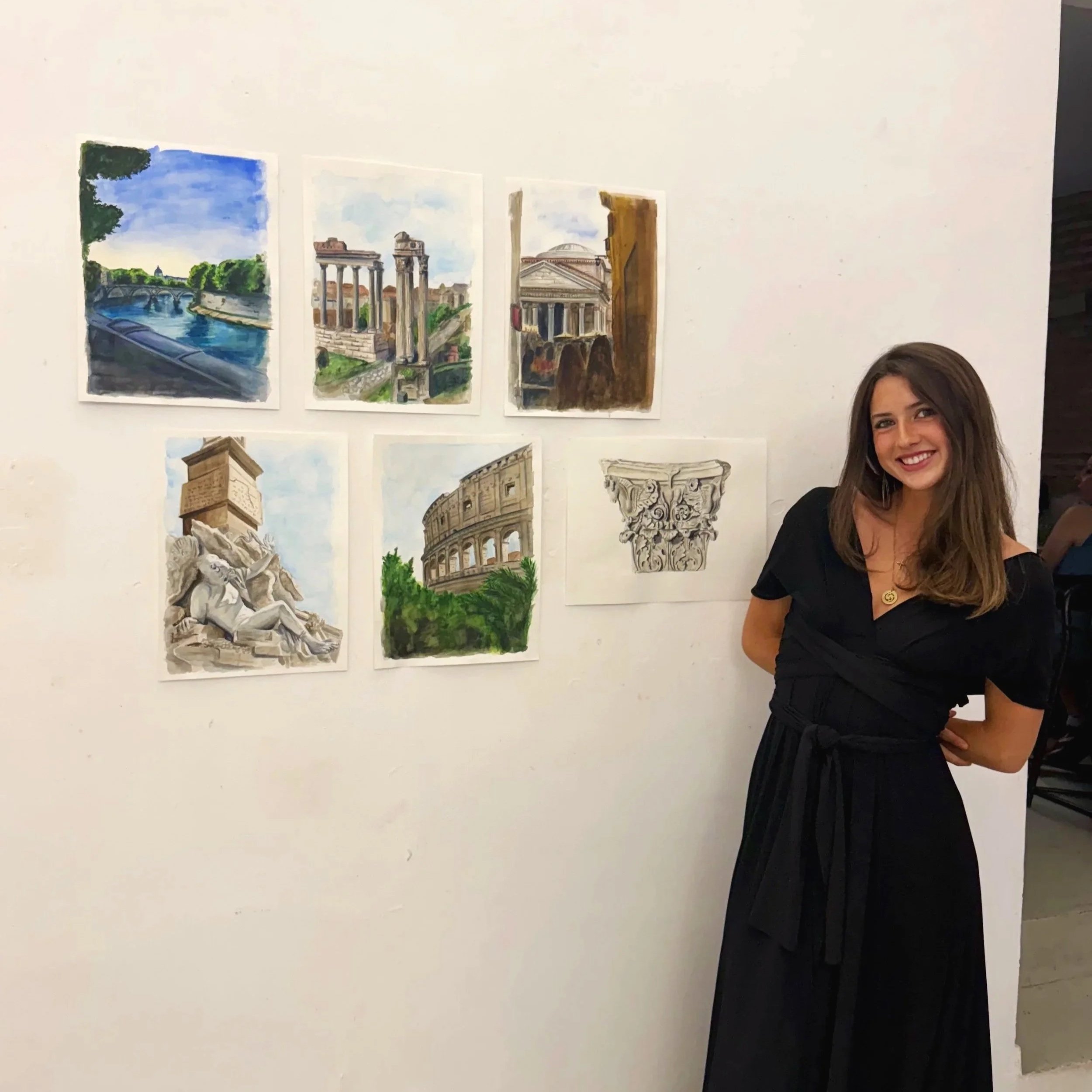 Watercolor paintings of ancient Roman and European architecture, displayed on a white wall, with a smiling woman standing nearby.