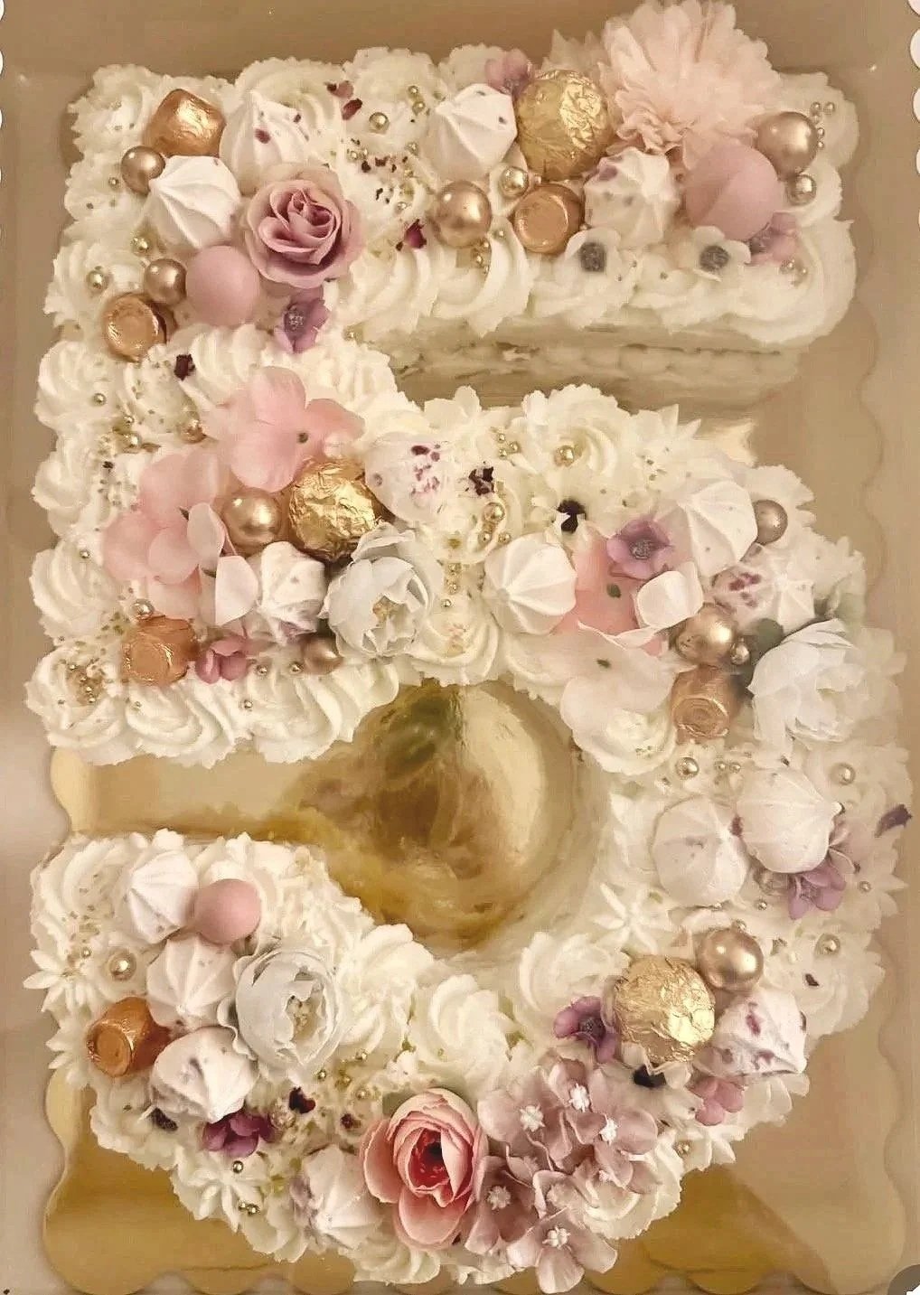 Decorative cake shaped like the Christ the Redeemer statue, decorated with pink and gold flowers, pearls, and meringue decorations.
