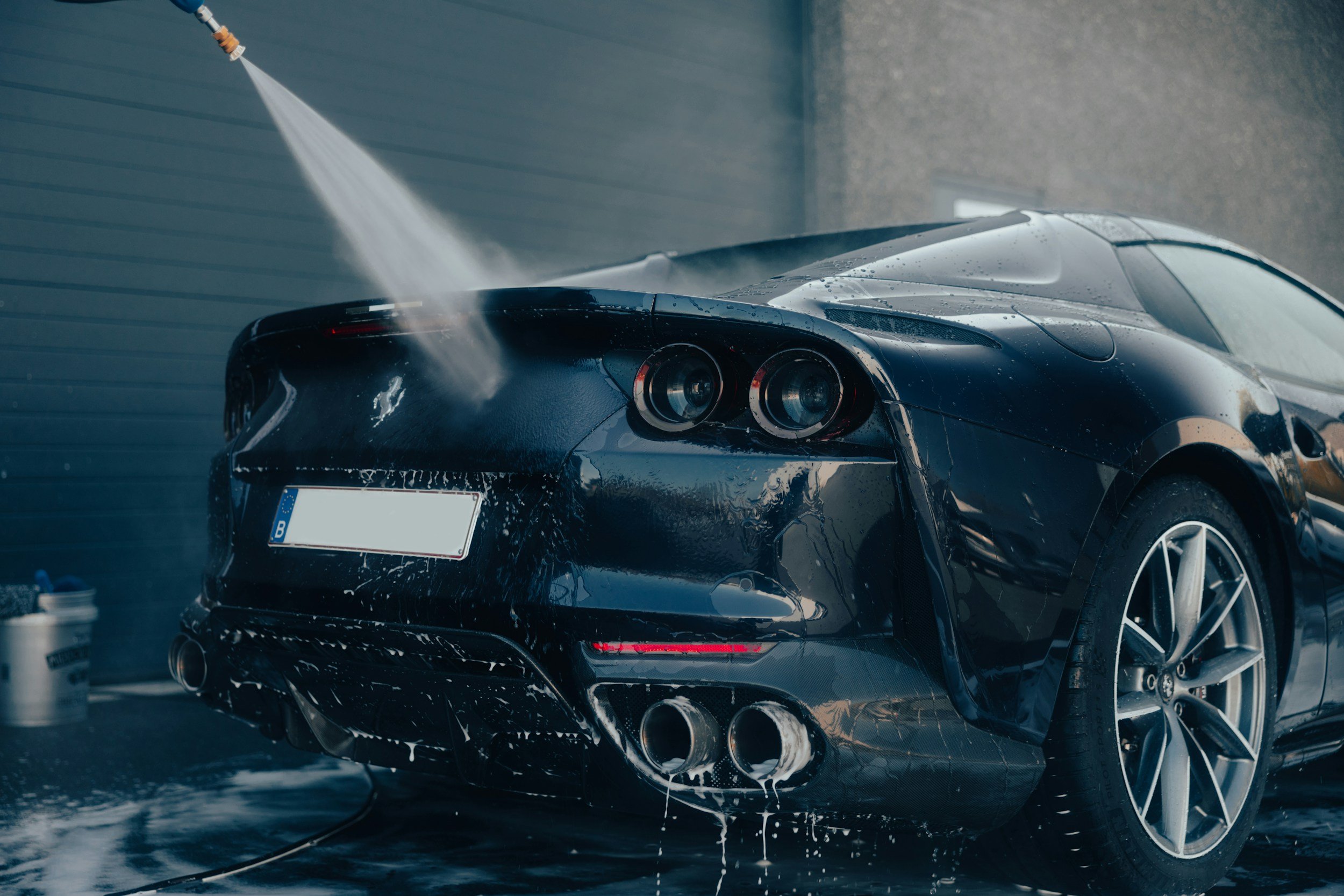 Black sports car being washed with a high-pressure water spray in a car wash station.
